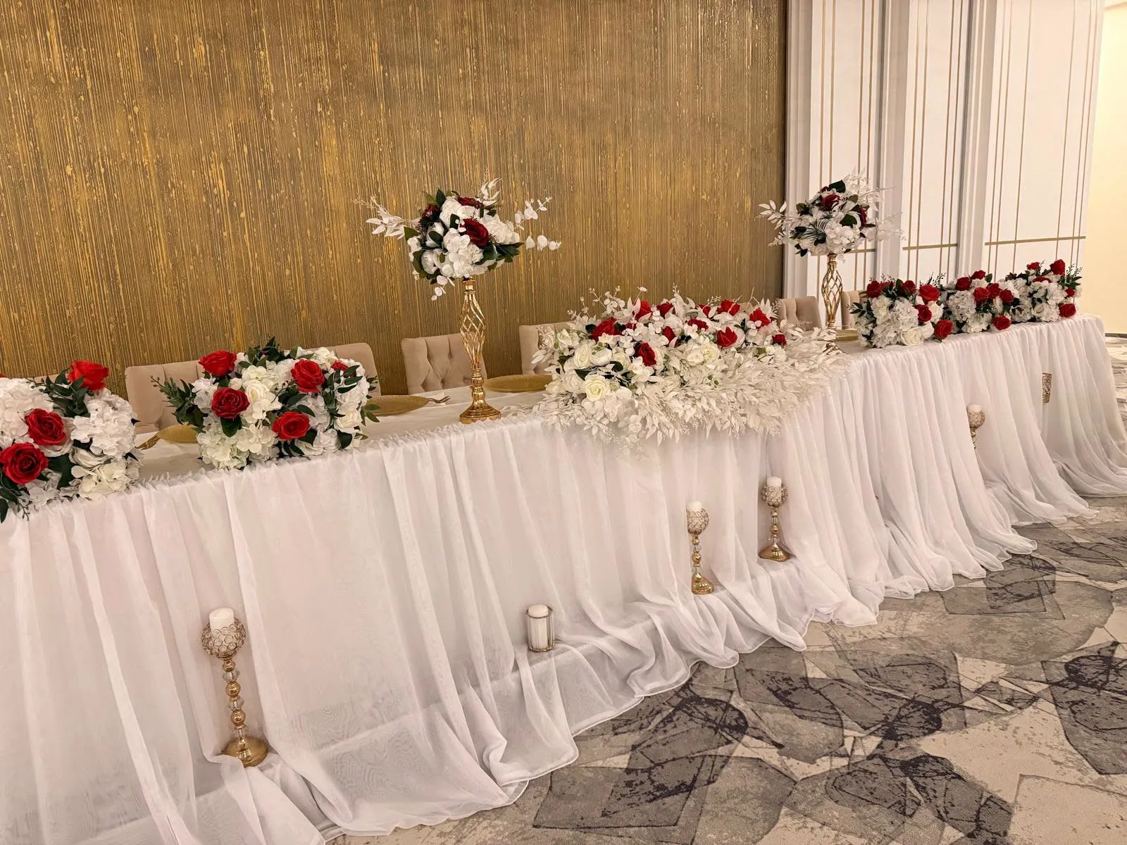 Prezidiu de nuntă în alb, cu aranjamente florale roșii și albe și draperie pe masă