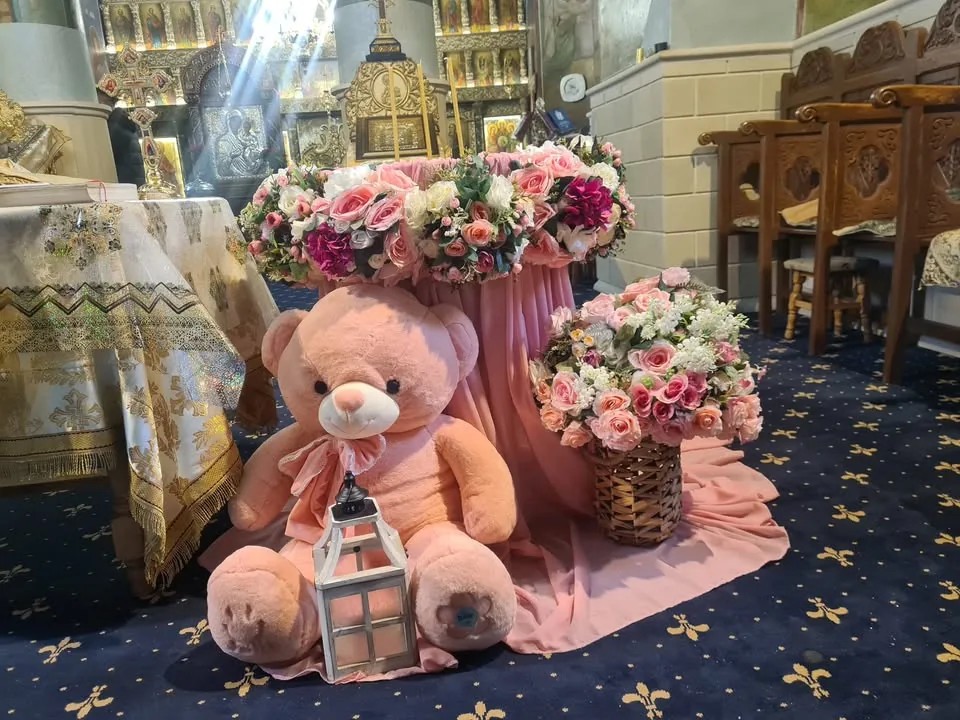 Decor de cristelniță în biserică, cu flori roz și albe și ursuleț de pluș