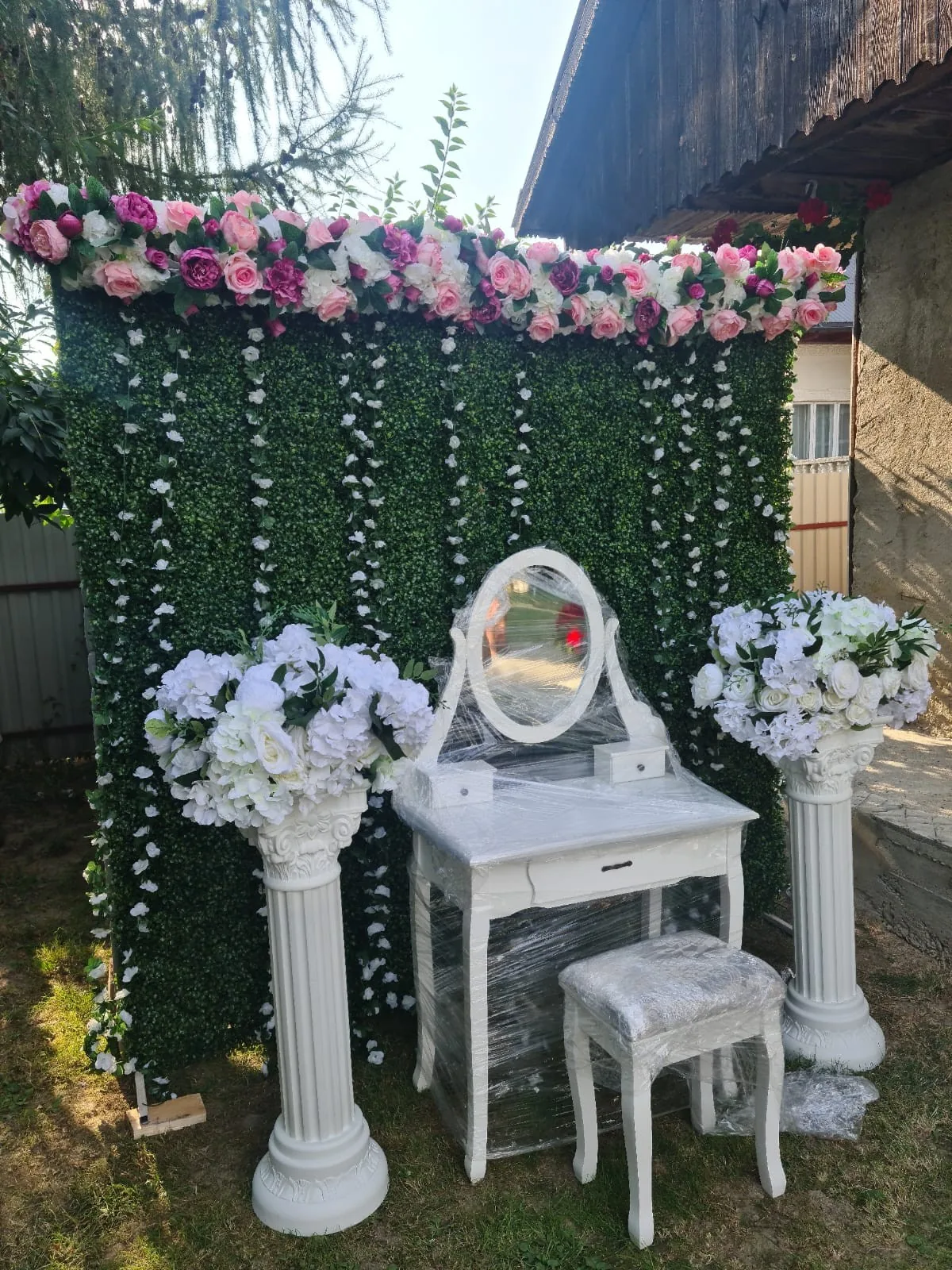 Decor pentru gătitul miresei acasă: perete verde cu flori roz și albe, oglindă ovală și coloane albe