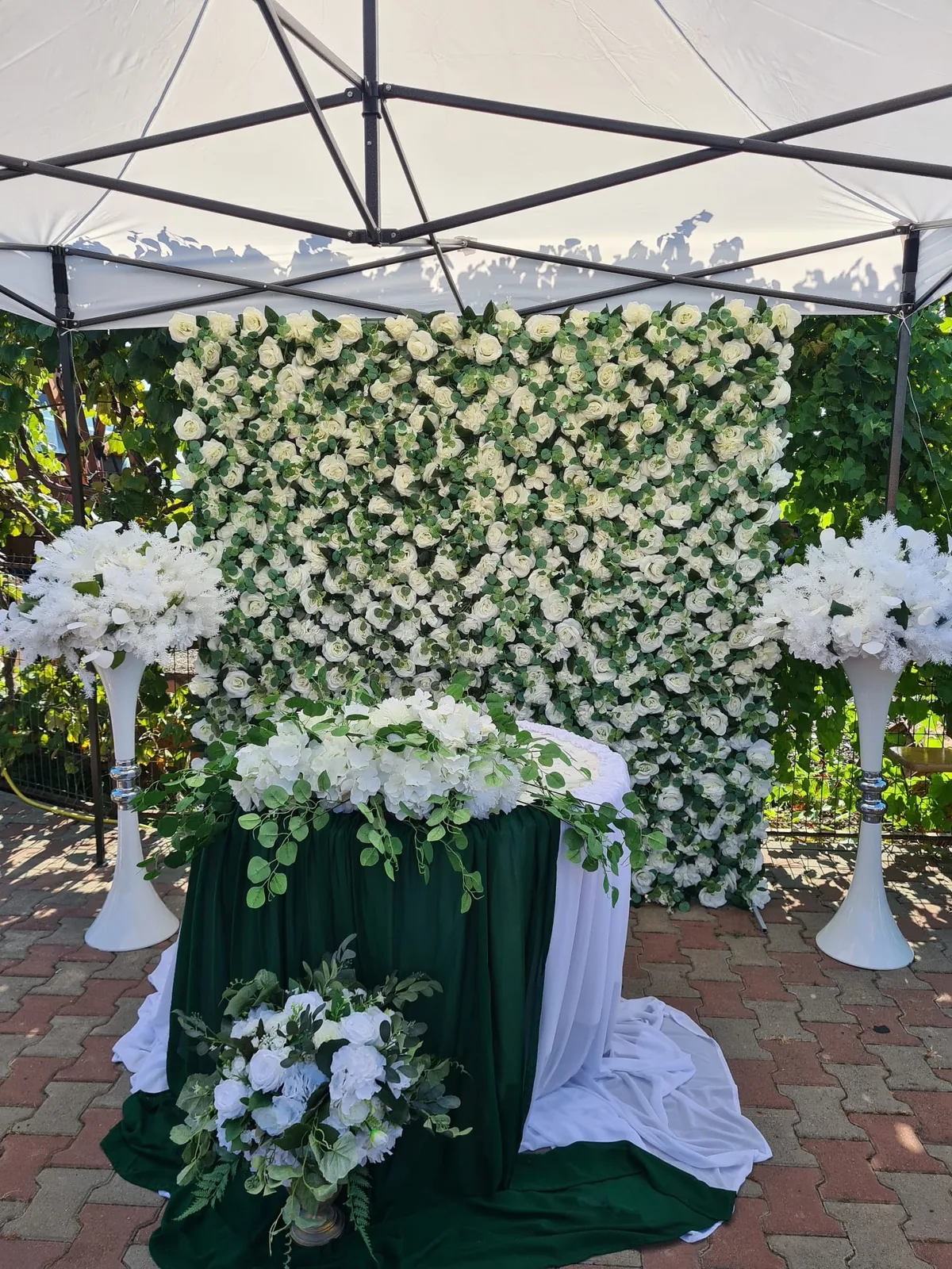 Perete floral alb-verde cu draperie verde și aranjamente pe suporturi înalte