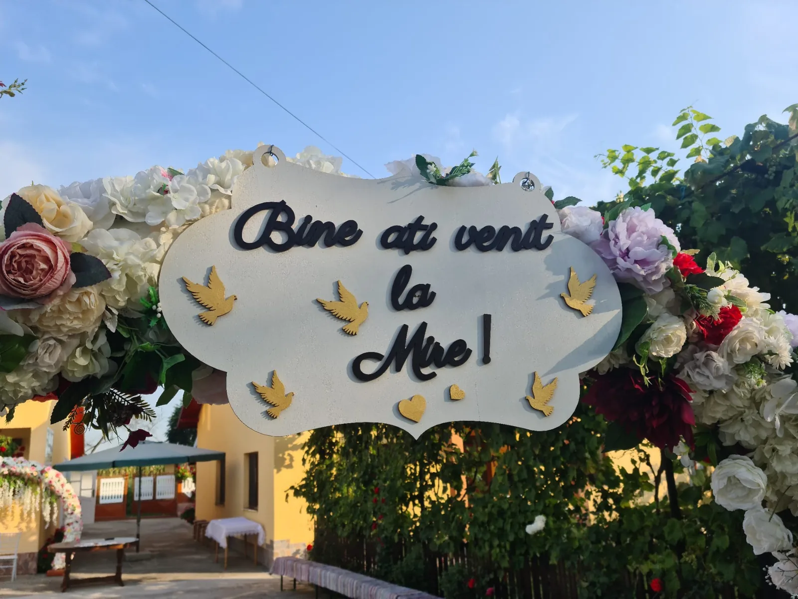 Plăcuță decorativă albă cu mesajul „Bine ați venit la Mire”, montată lângă decorul floral