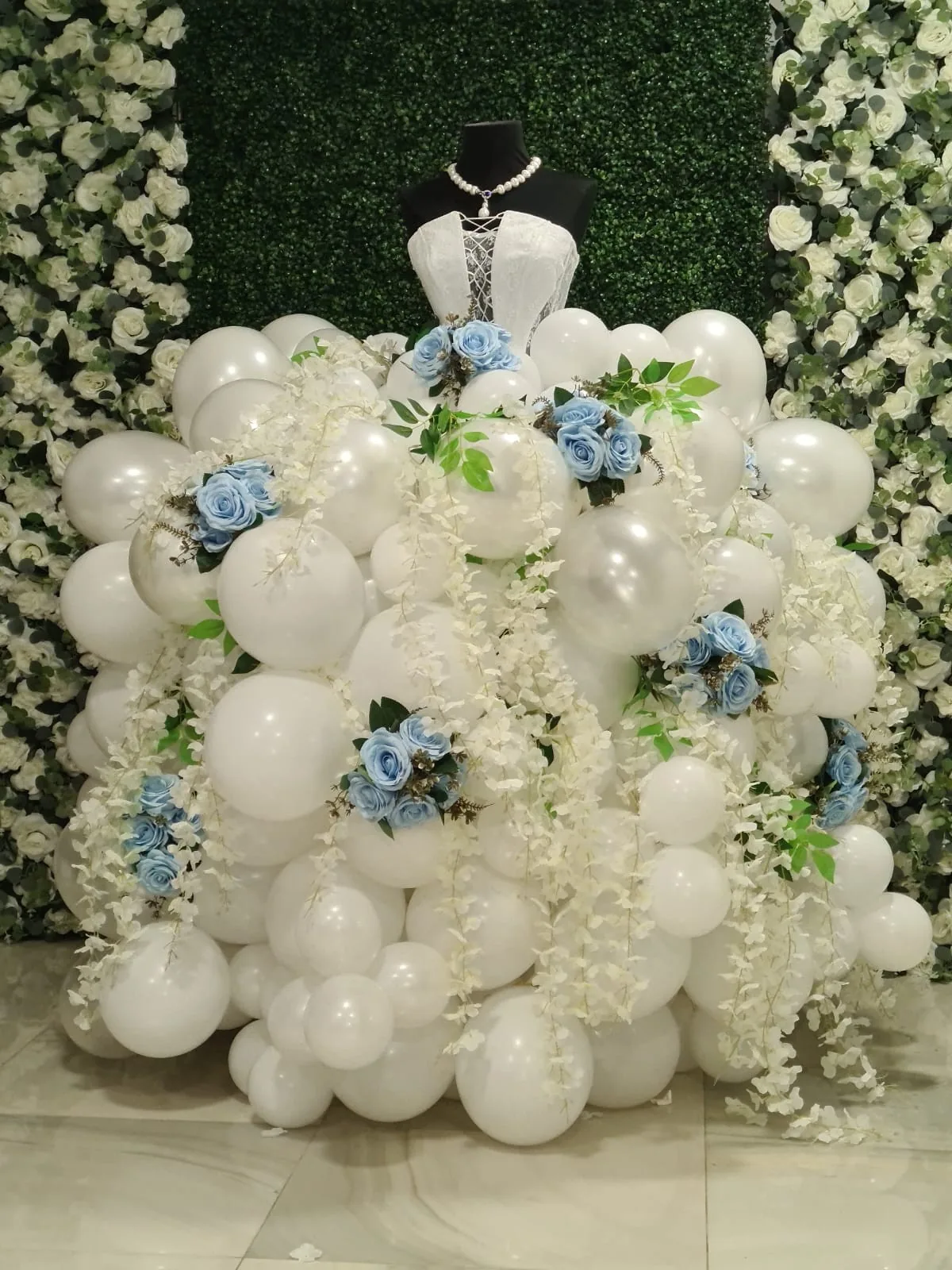 Rochie din baloane albe și flori bleu, expusă pe perete floral