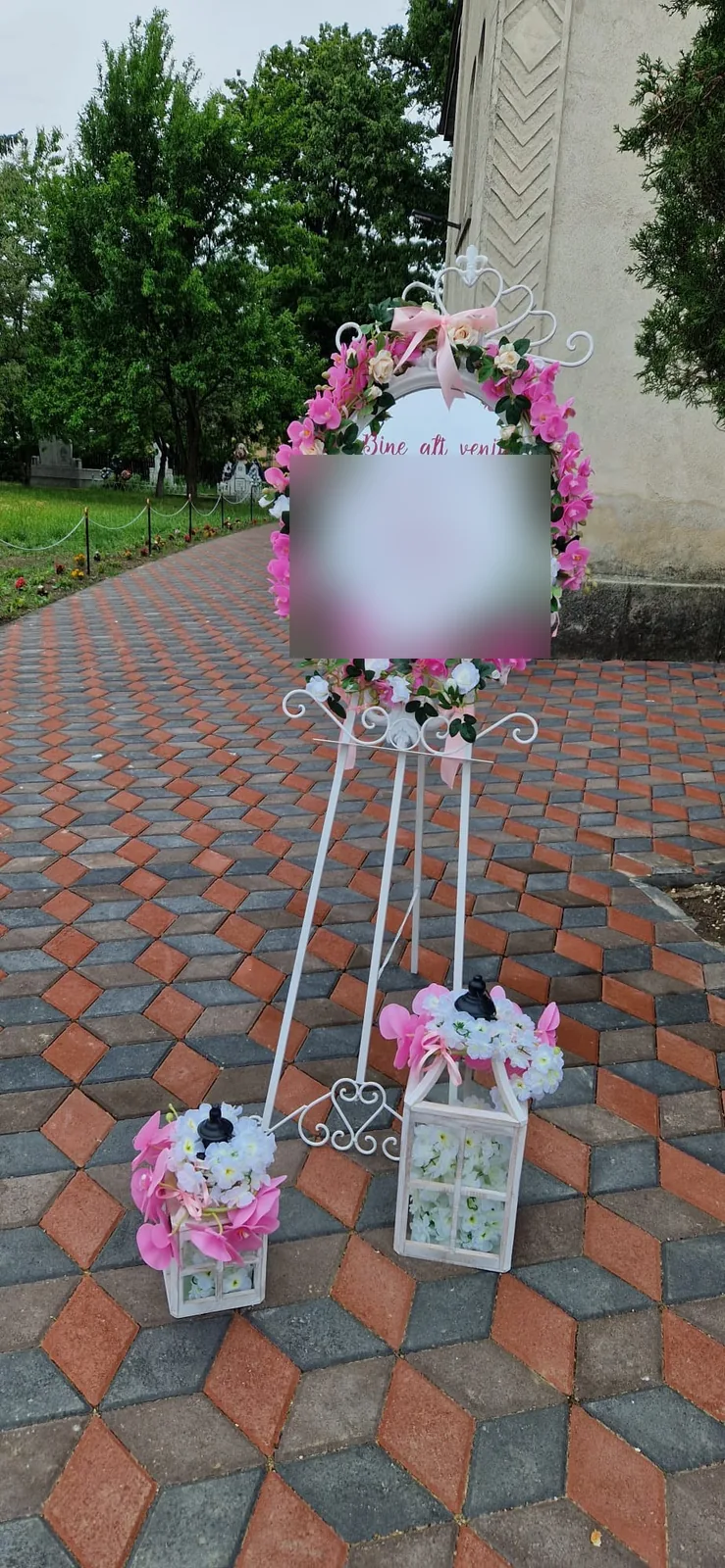 Șevalet de botez cu coroniță de flori roz și albe, pe alee