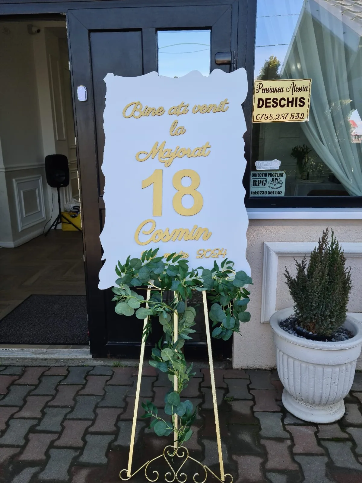 Șevalet de majorat cu panou alb și cifra 18, decorat cu verdeață