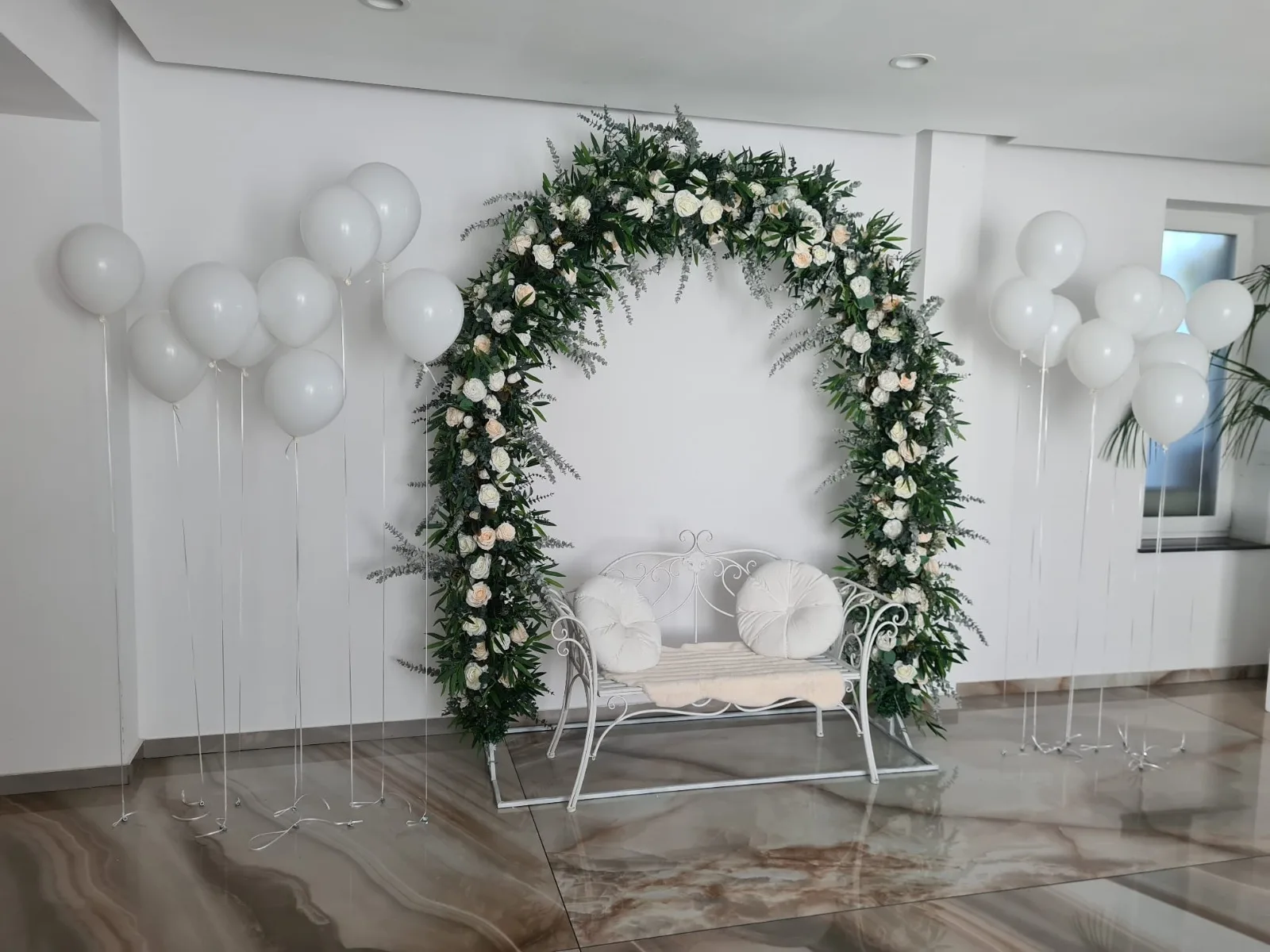 Grupuri de baloane albe cu heliu de o parte si de alta a unei arcade circulare florale cu canapea alba