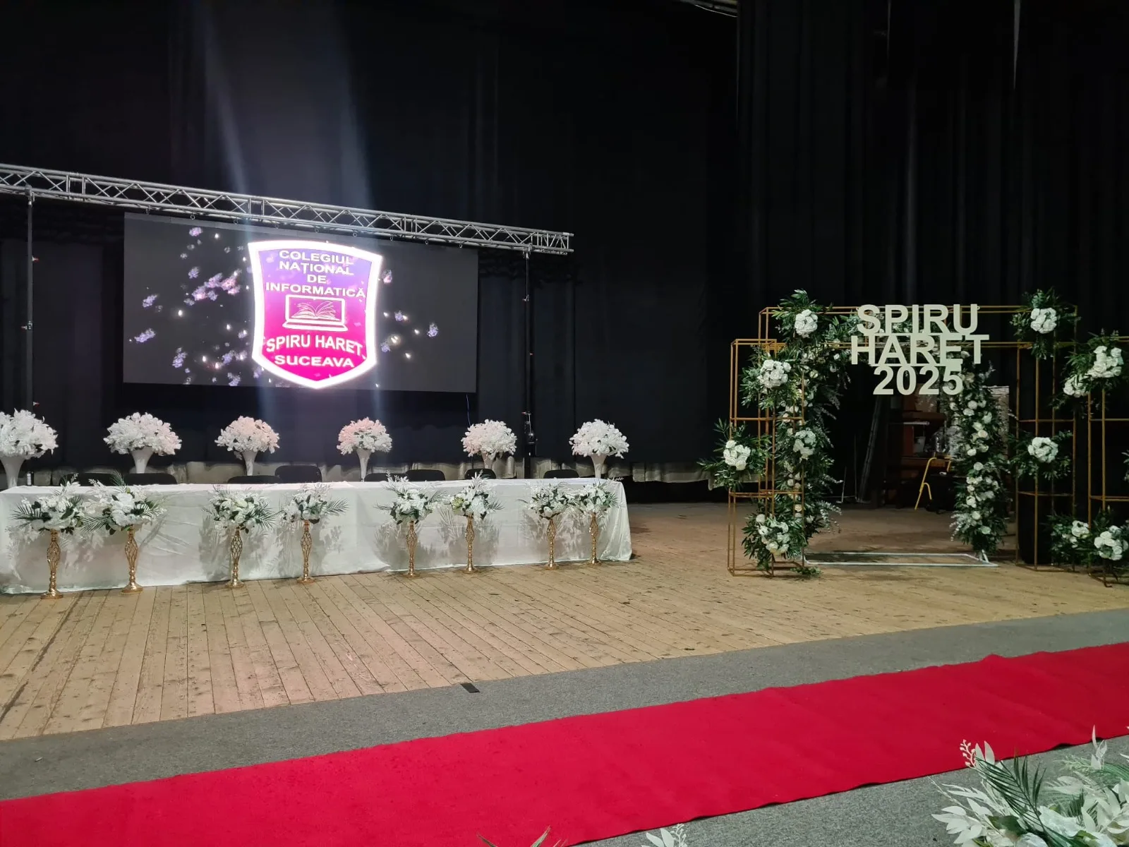 Scena cu prezidiu si flori albe, covor rosu, banner Spiru Haret 2025 pe ecran