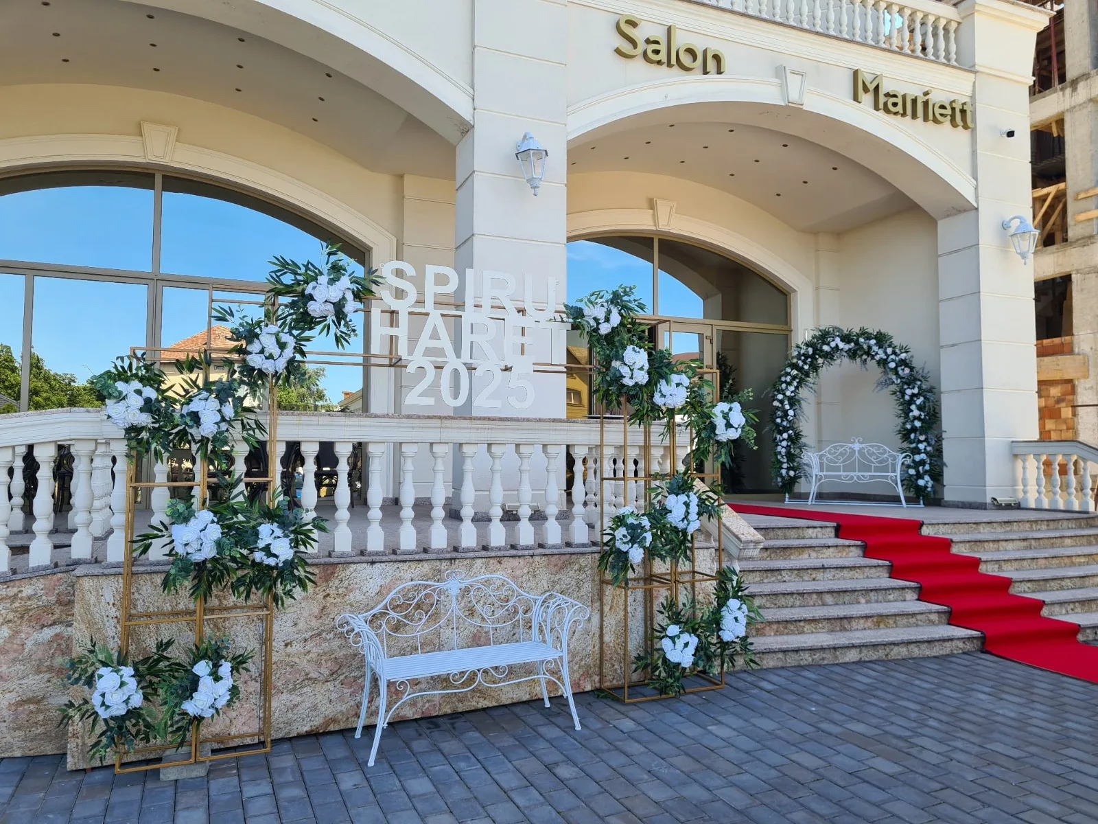 Arcadă cu flori albe si verdeata la intrarea in salon, cu covor rosu si banca alba decorativa