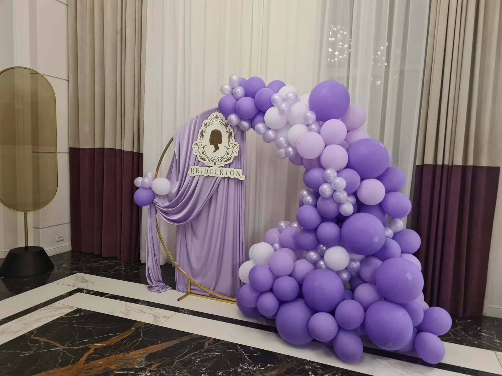 Decor tematic Bridgerton cu draperie mov si arcada de baloane mov, fundal cu oglinda si cortine