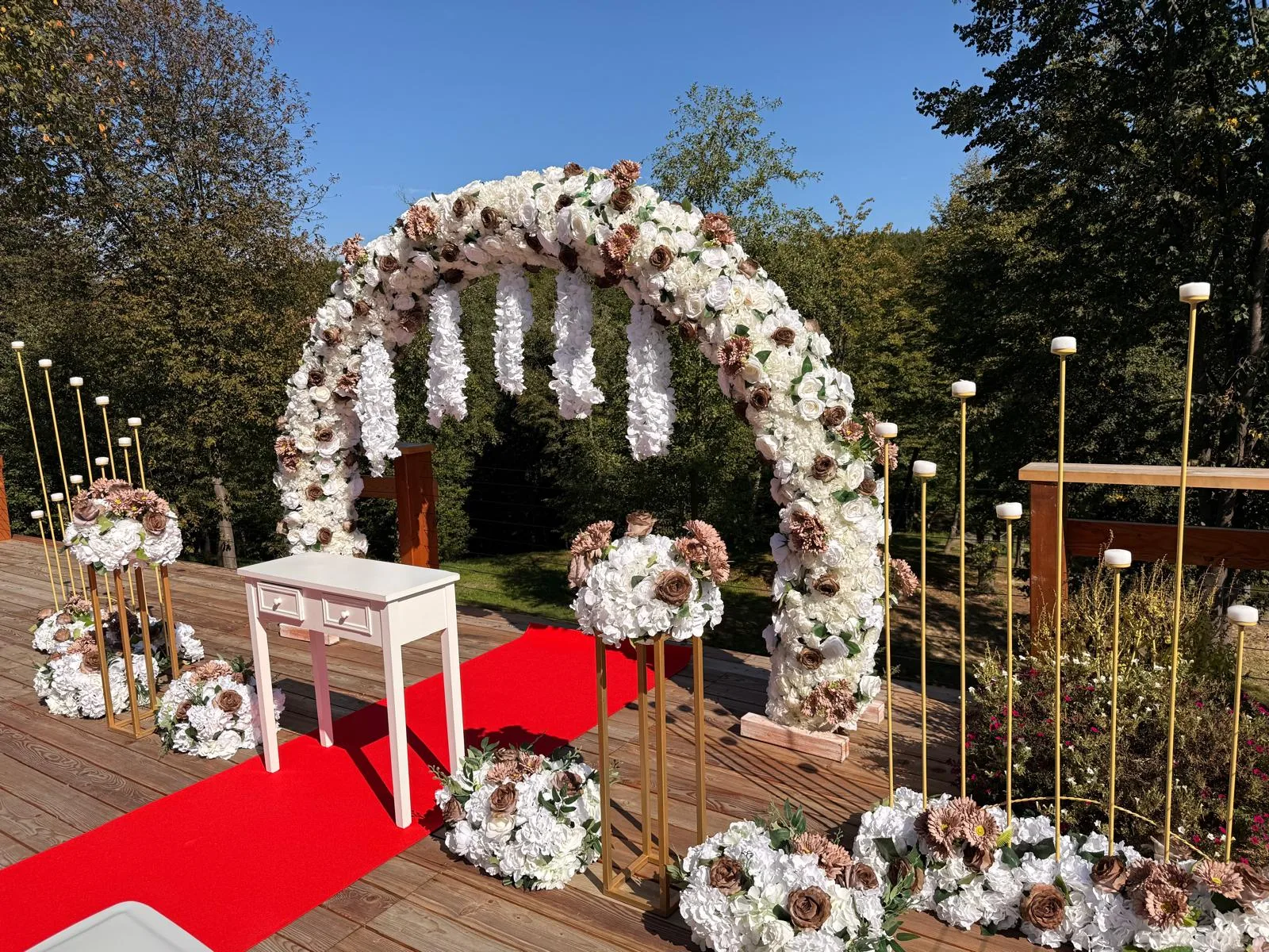 Arcadă florală albă cu masă de oficiere și covor roșu, decor cununie civilă pe terasă de lemn
