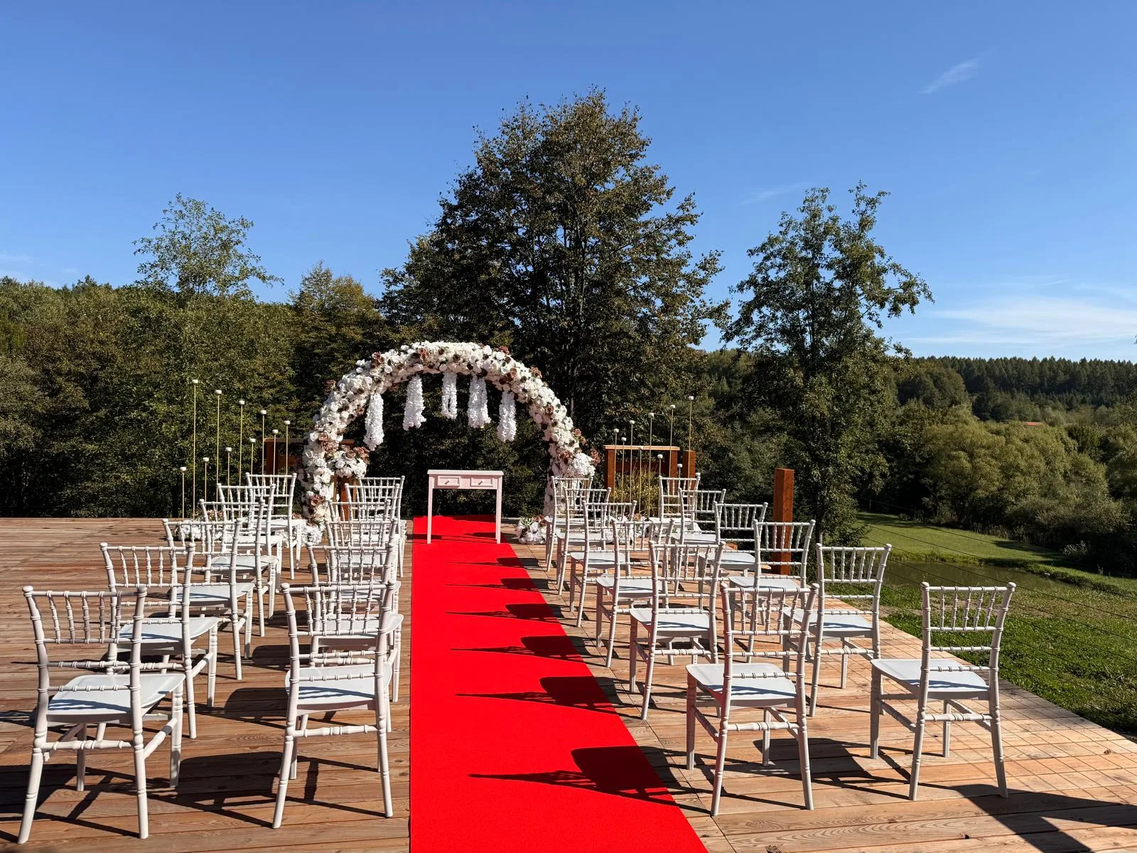 Culoar cu scaune Chiavari albe și covor roșu spre arcada florală, decor cununie civilă în natură