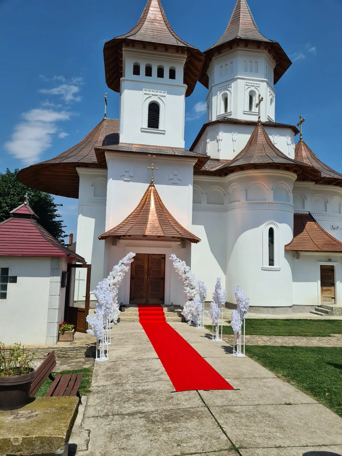 Fațada bisericii cu turnuri, cer senin și covor roșu spre intrare