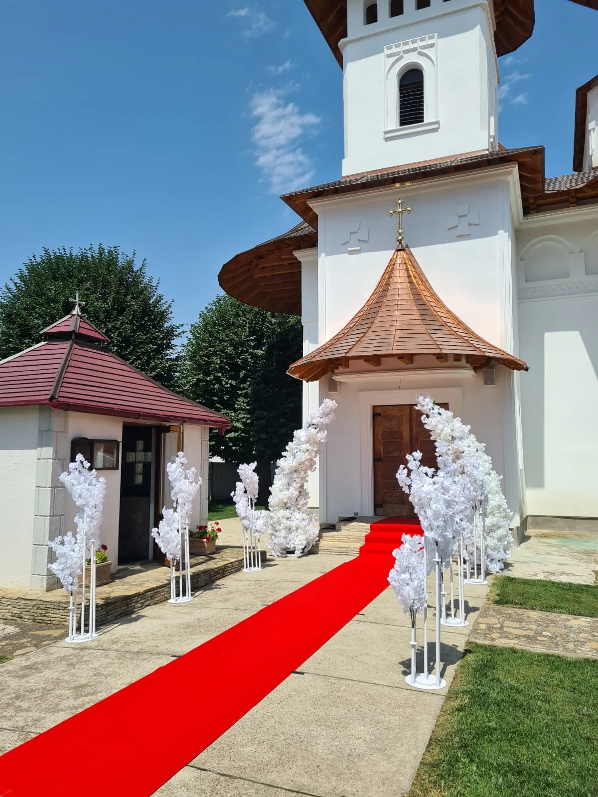 Turnurile bisericii cu copaci decorativi albi și covor roșu pe alee