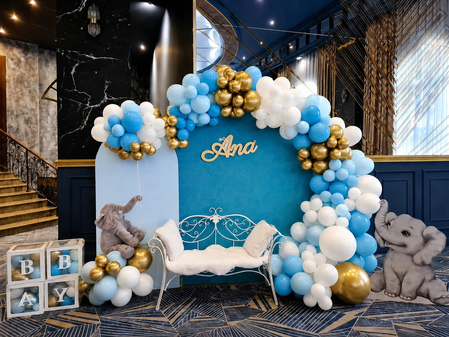 Photocorner de botez albastru cu auriu, elefănței decorativi, bancă albă și panoul cu numele Ana