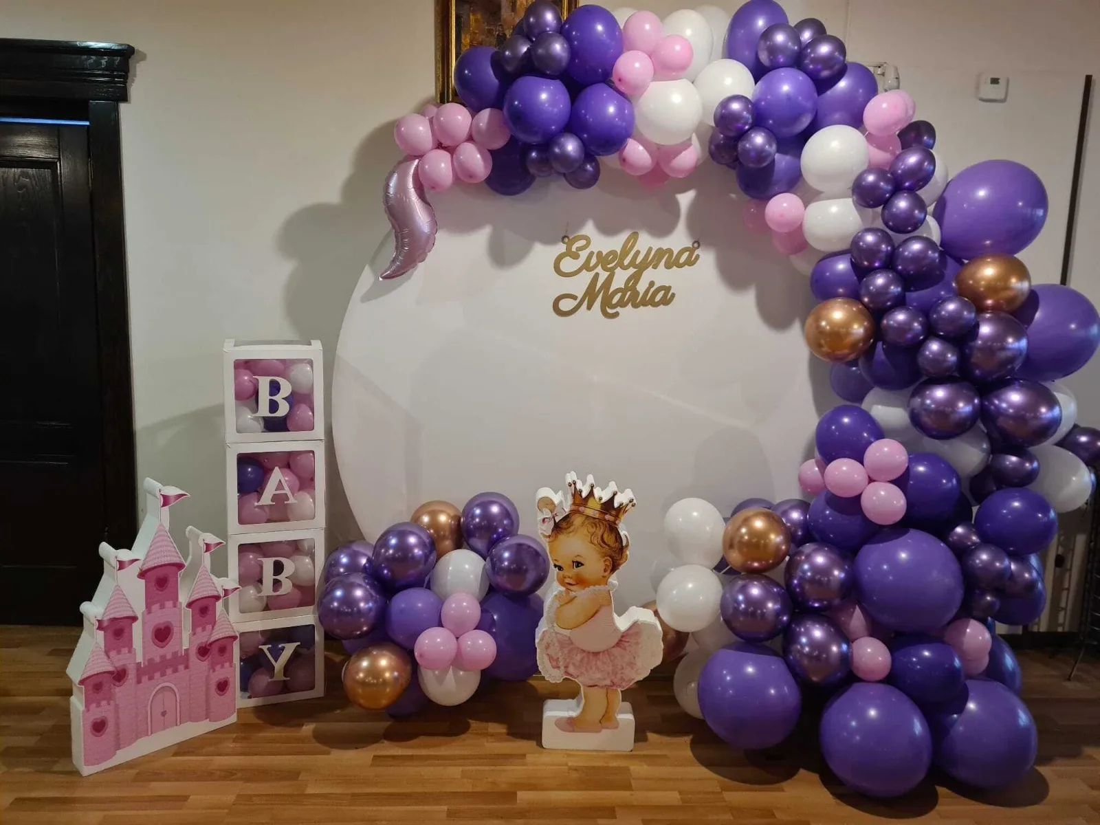 Arcadă de baloane mov, albe și aurii cu castel decorativ roz și siluetă fetiță cu coroniță, numele Evelyna Maria
