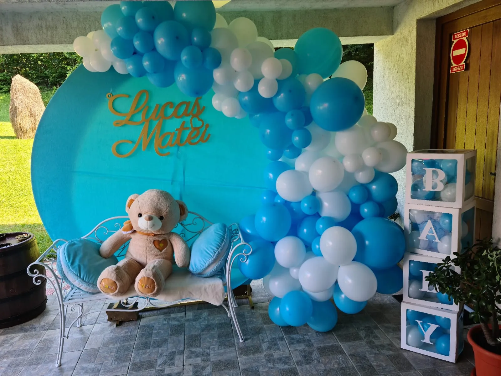 Photocorner de botez turcoaz și alb, ursuleț de pluș pe bancă, panoul cu numele Lucas Matei