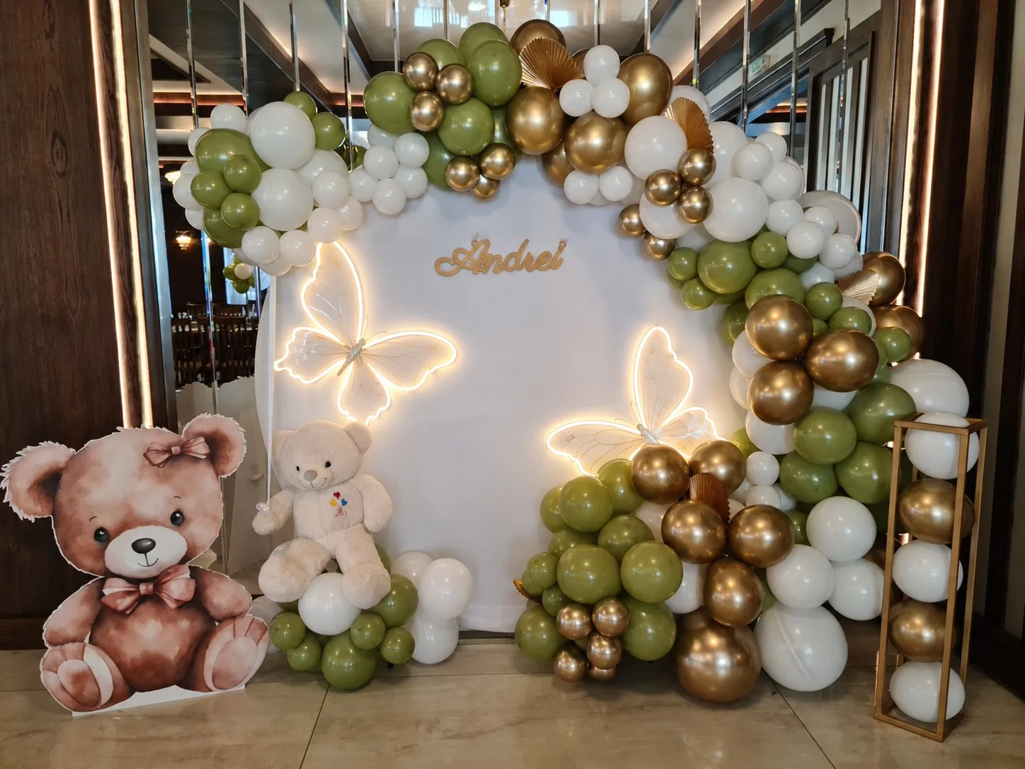 Photocorner de botez verde cu auriu, fluturi luminoși și ursuleți de pluș, panoul cu numele Andrei