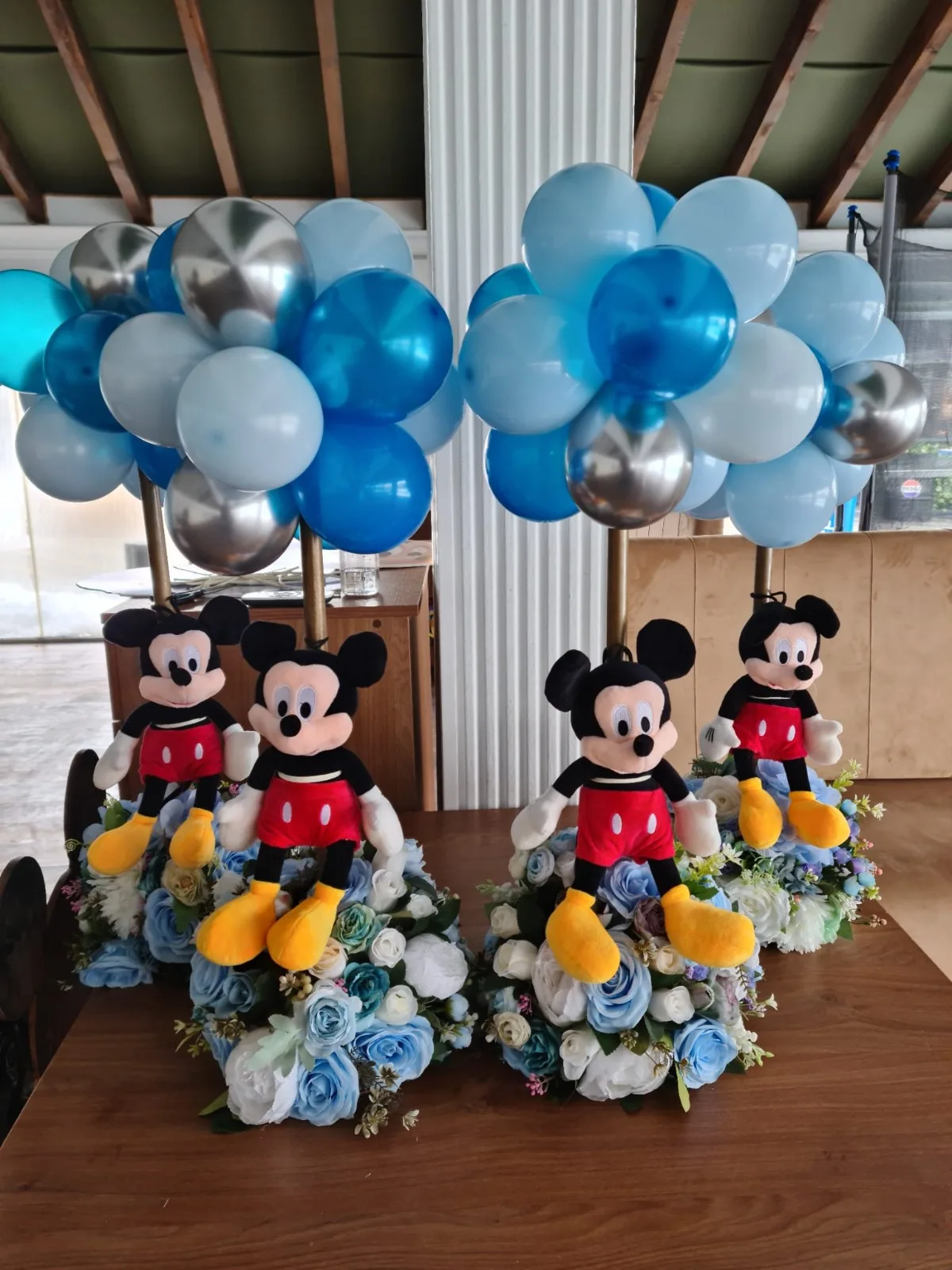 Centru de masă cu jucării Mickey Mouse de pluș și flori albastre și albe, patru aranjamente pe o masă