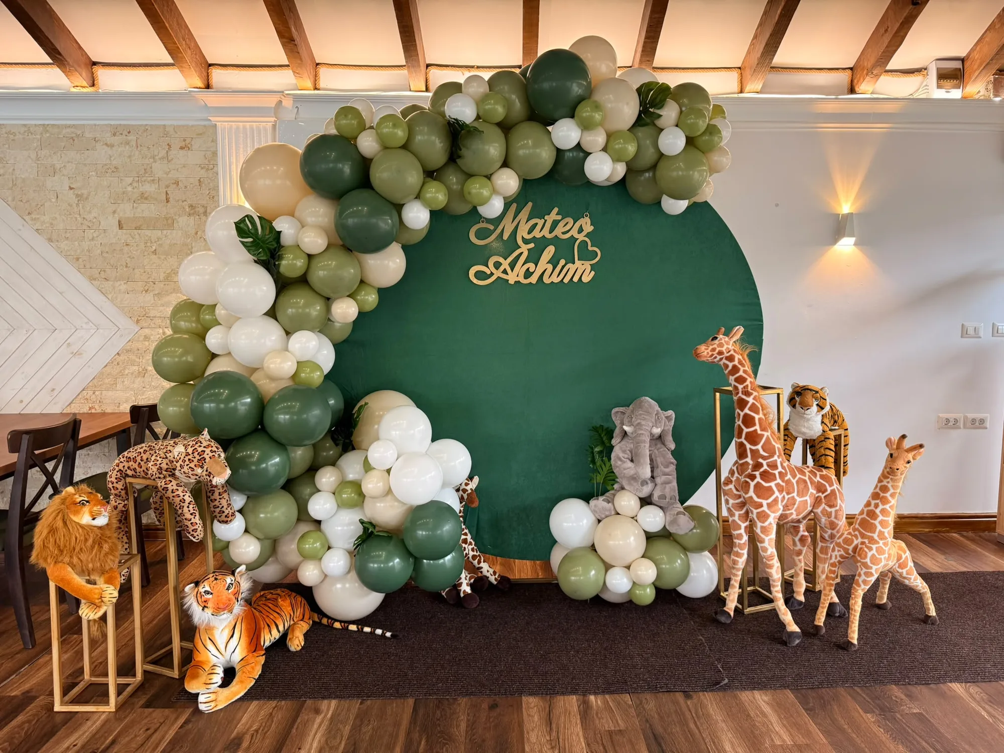Decor botez tematic jungle, cu arcada de baloane verzi si crem, panou verde cu numele copilului si figurine de animale de plus