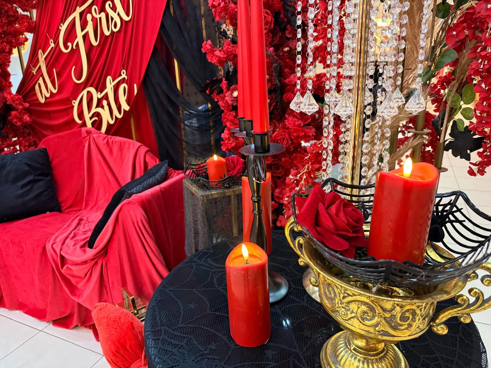 Masuta neagra cu lumanari rosii aprinse si cupa aurie cu trandafiri, decor corporate Halloween
