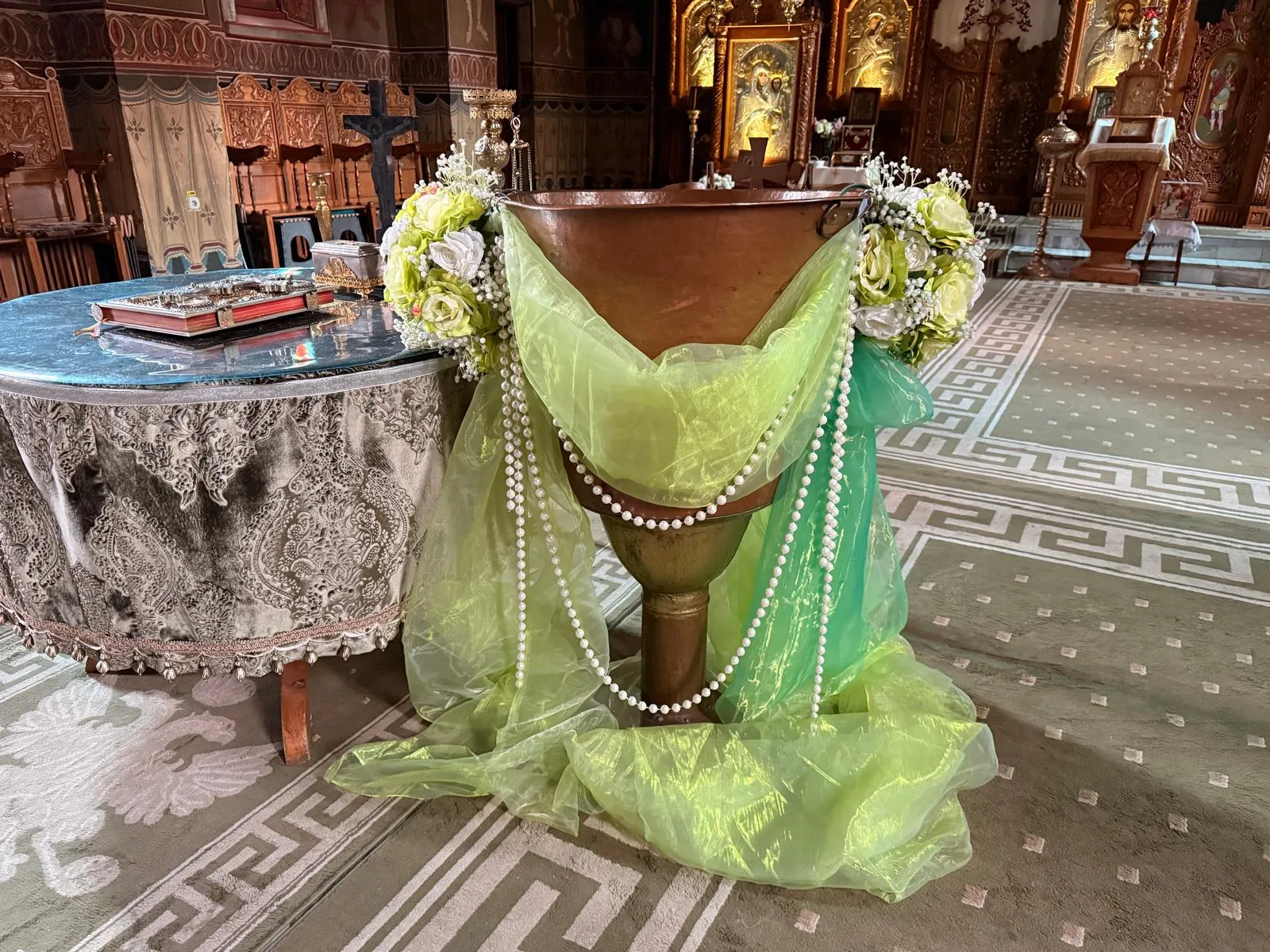 Decor de cristelniță în biserică, cupă din aramă cu tul alb, lanț de perle și aranjament de trandafiri albi
