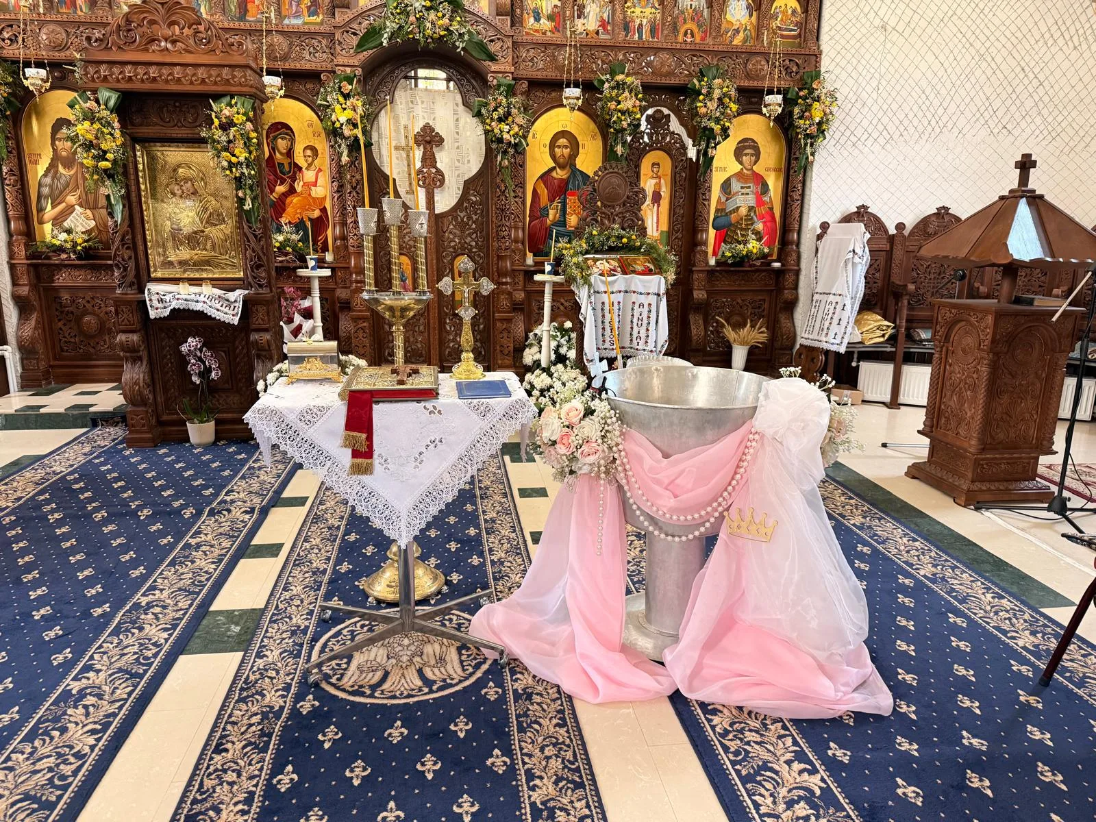 Masă de altar cu Sfânta Evanghelie și cristelniță decorată cu tul roz și verde, în biserică
