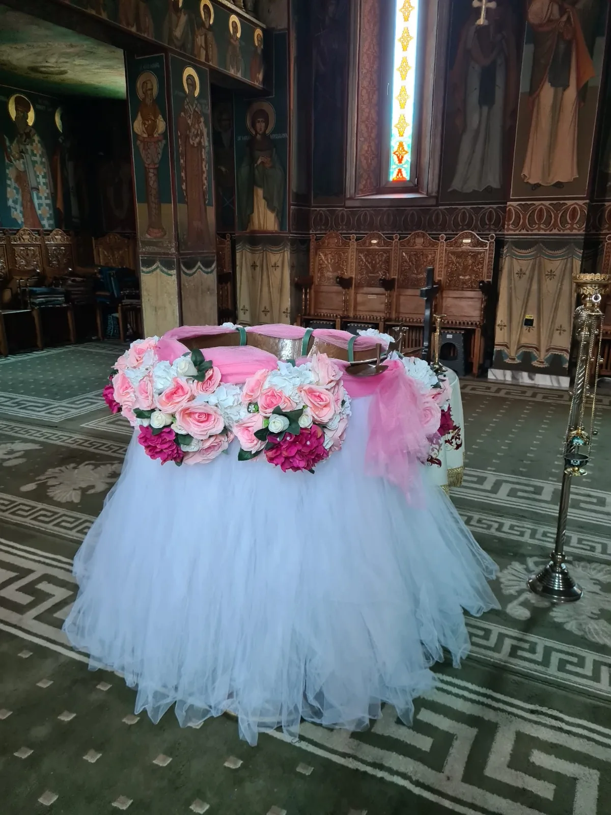 Decor de cristelniță în biserică, cu tul alb, coroniță de flori roz și eșarfă roz