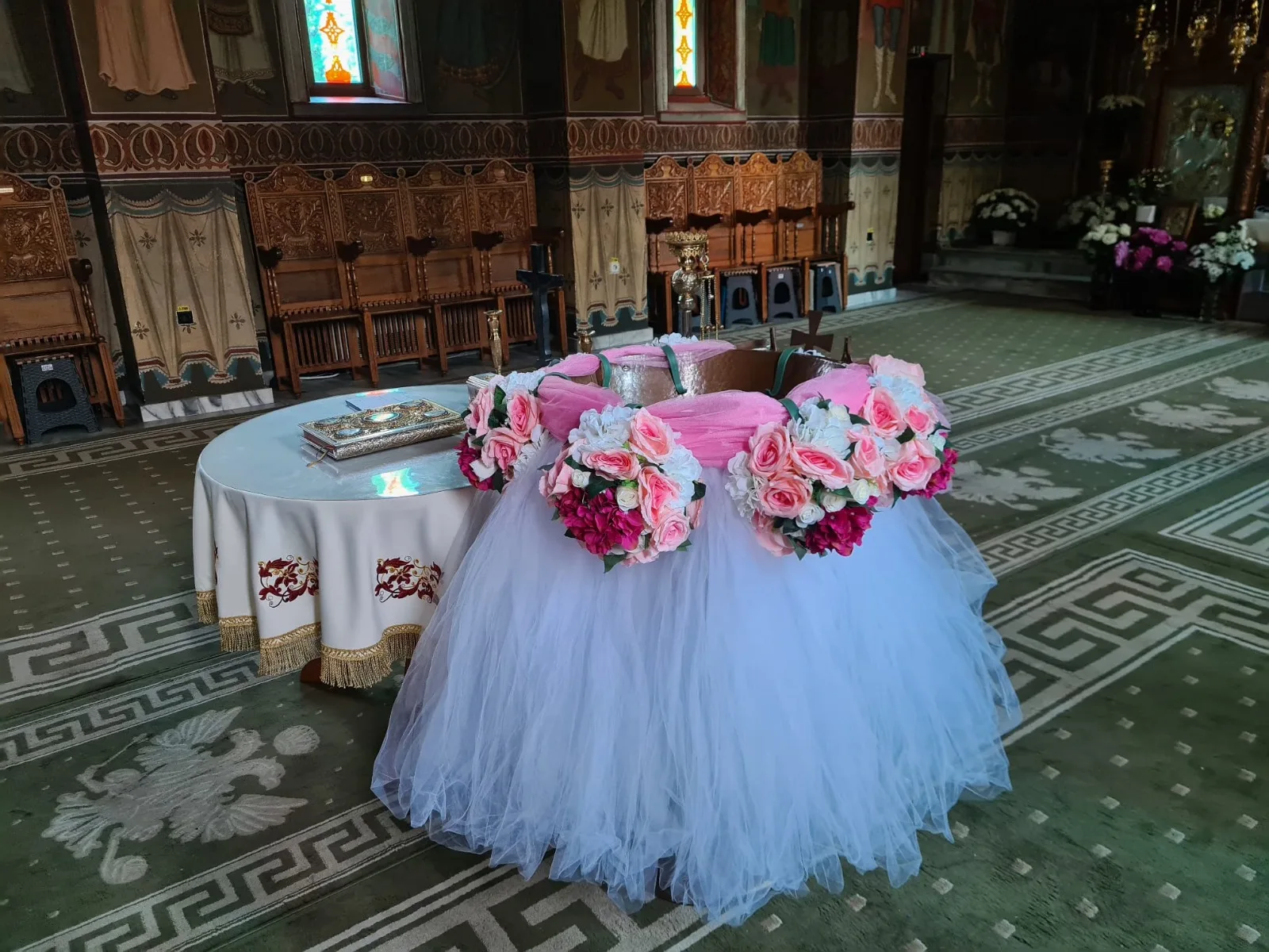Decor de cristelniță în biserică, cu tul alb și coroniță de flori roz și albe