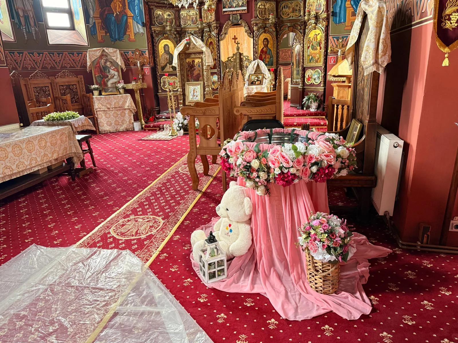 Cristelniță decorată cu tul roz și flori, în interiorul bisericii, cu ursuleț de pluș alături
