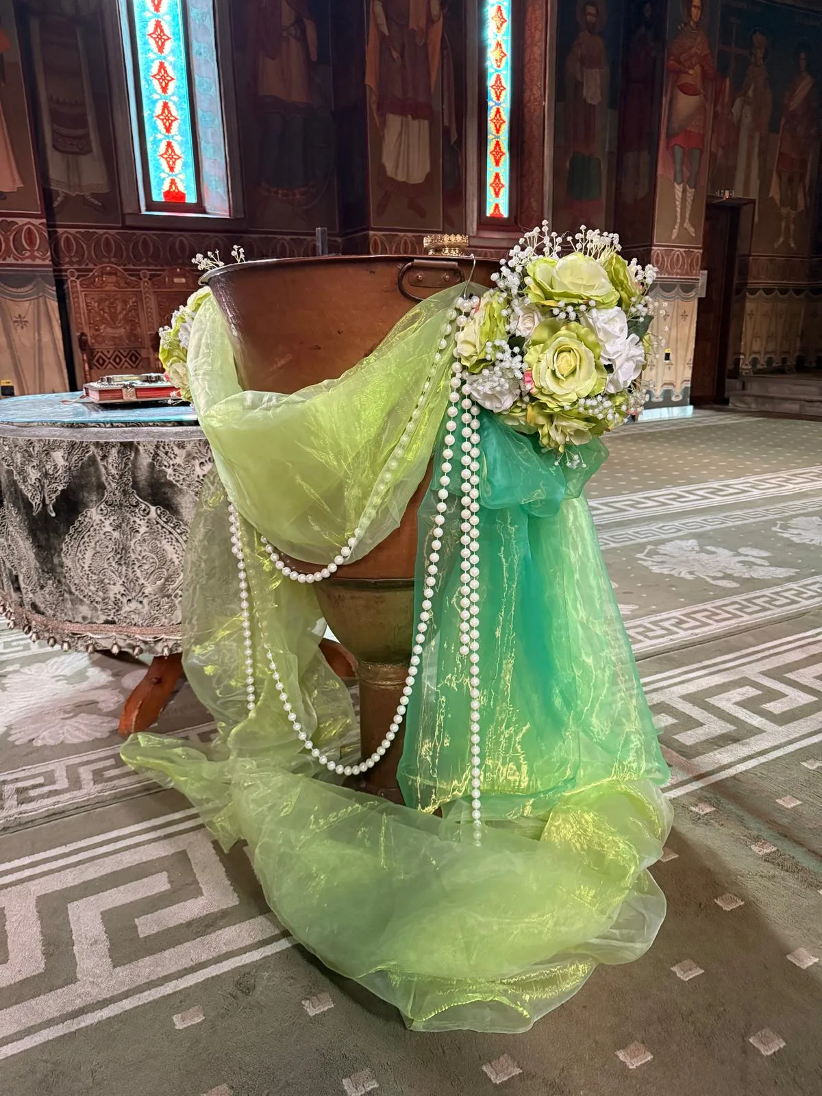 Cupă de cristelniță în biserică, cu tul verde pastel, lanț de perle și coroniță de trandafiri galbeni și albi