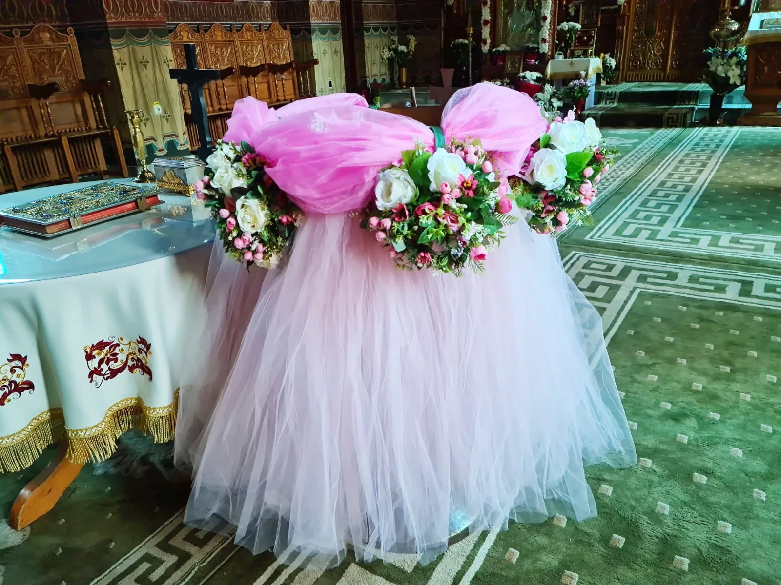 Decor de cristelniță în biserică, cu tul roz și coronițe de flori albe și roz
