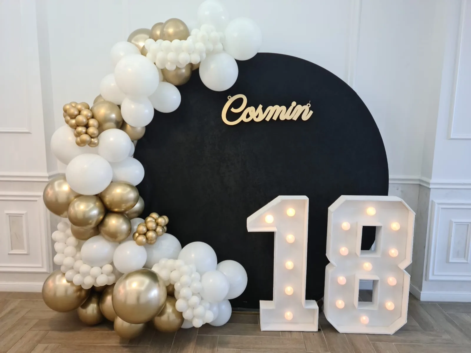 Decor majorat 18 ani cu backdrop negru, nume Cosmin, cifre luminoase 18 si baloane alb-auriu