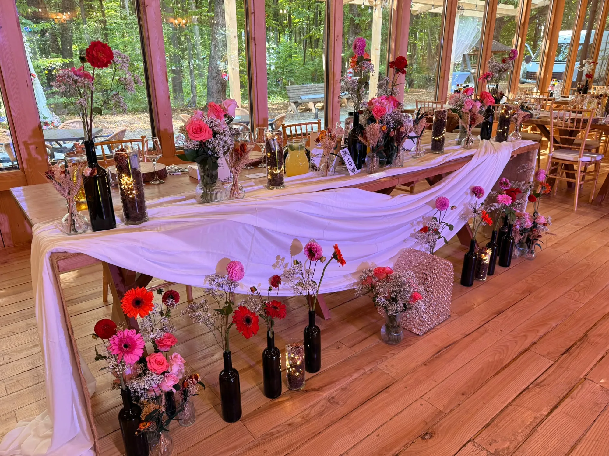 Masă lungă de nuntă cu decor floral și sticle cu flori