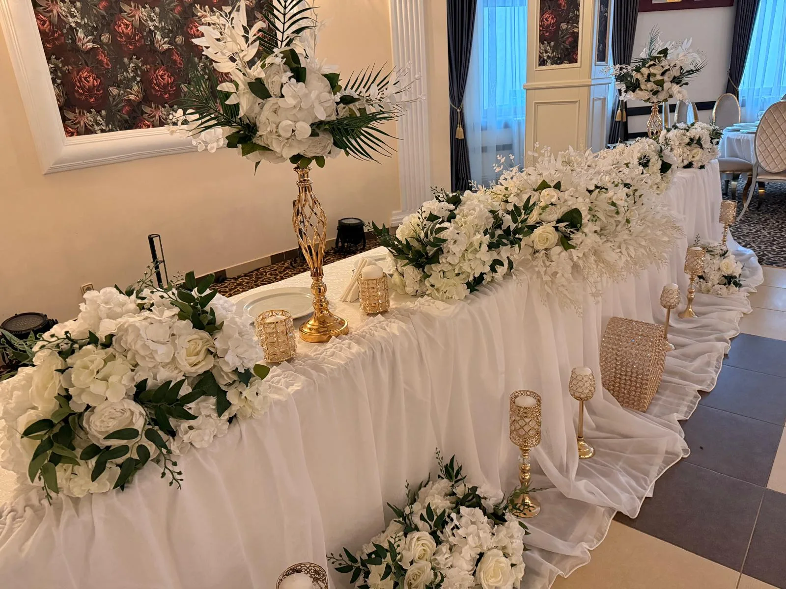 Masa oficialilor decorată cu flori albe, verdeață și sfeșnice aurii de cristal