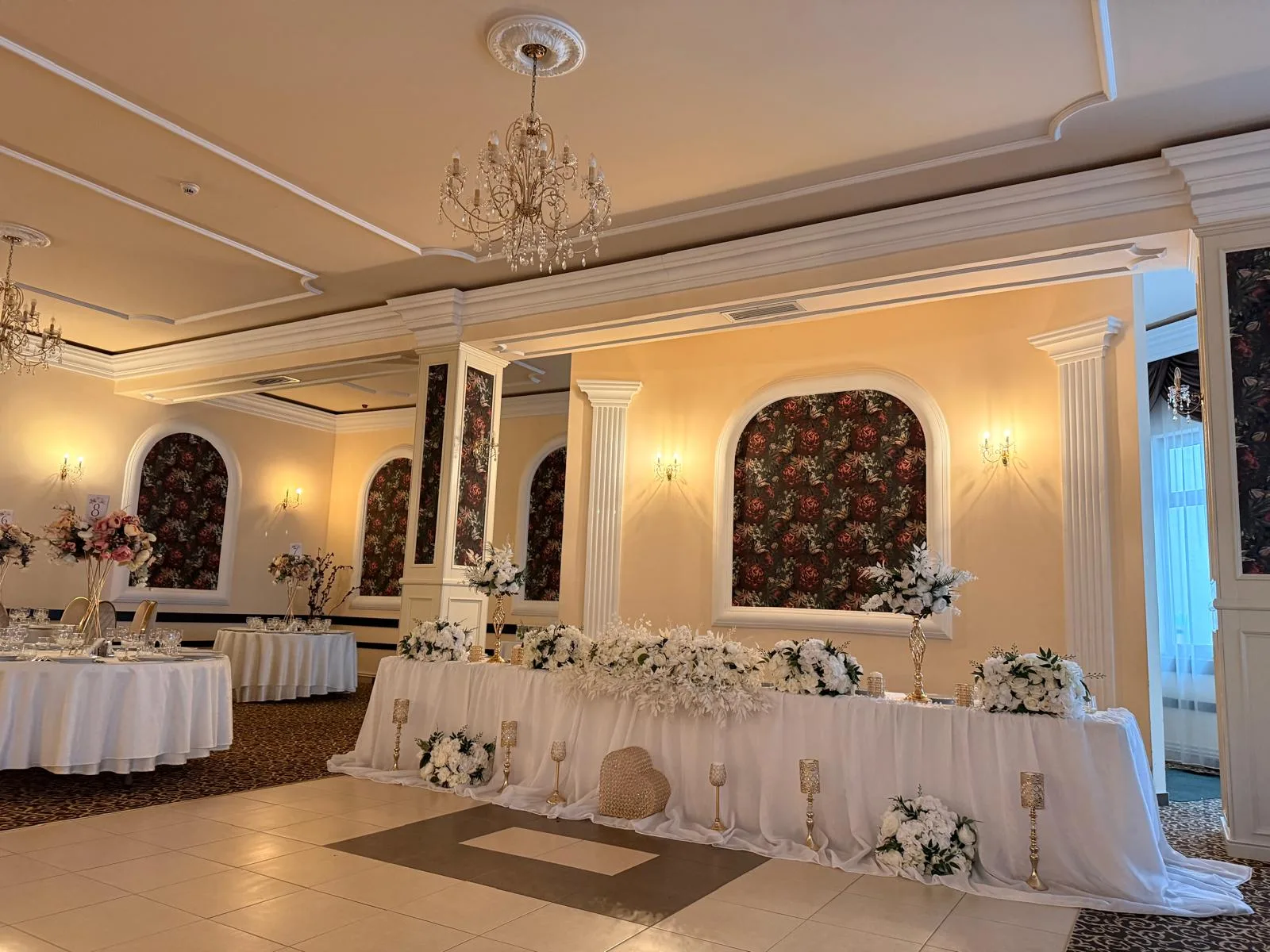 Prezidiu de nuntă alb cu aranjamente florale aurii și candelabru de cristal suspendat