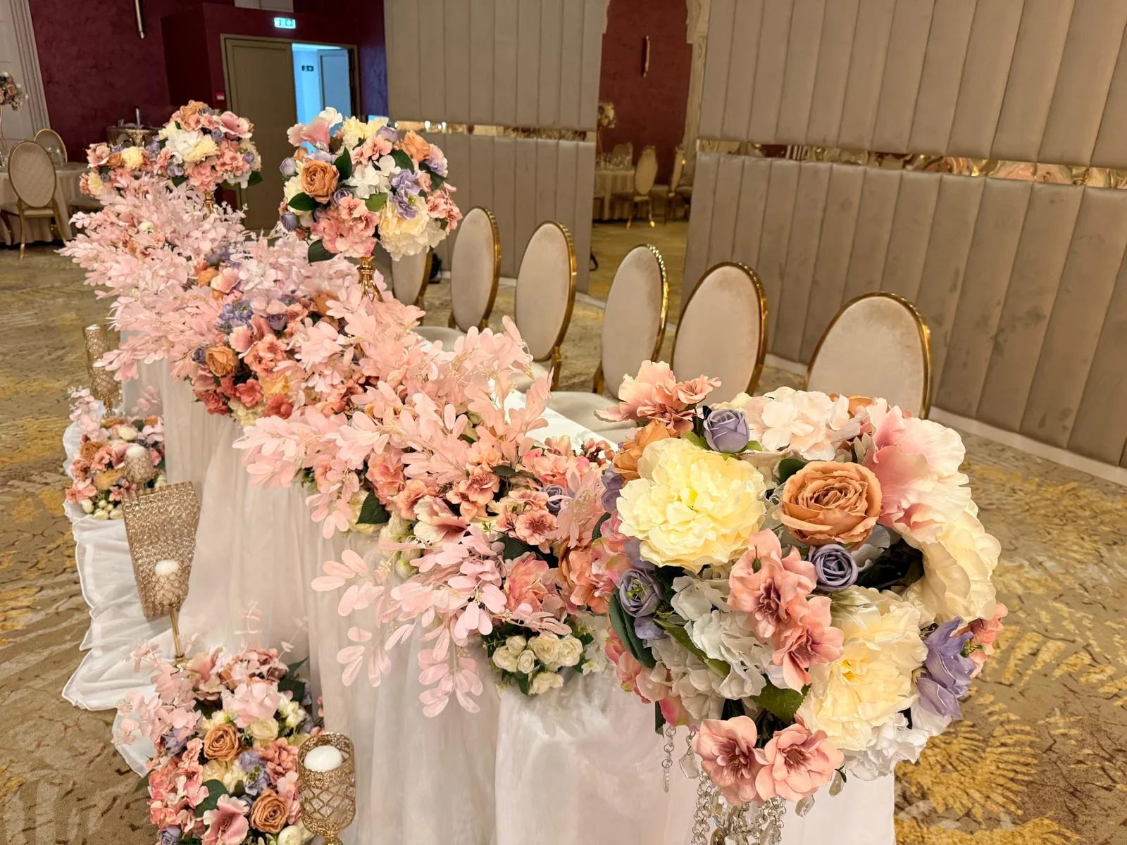 Prezidiu de nuntă lung cu aranjamente florale în nuanțe de roz, piersică și lavandă