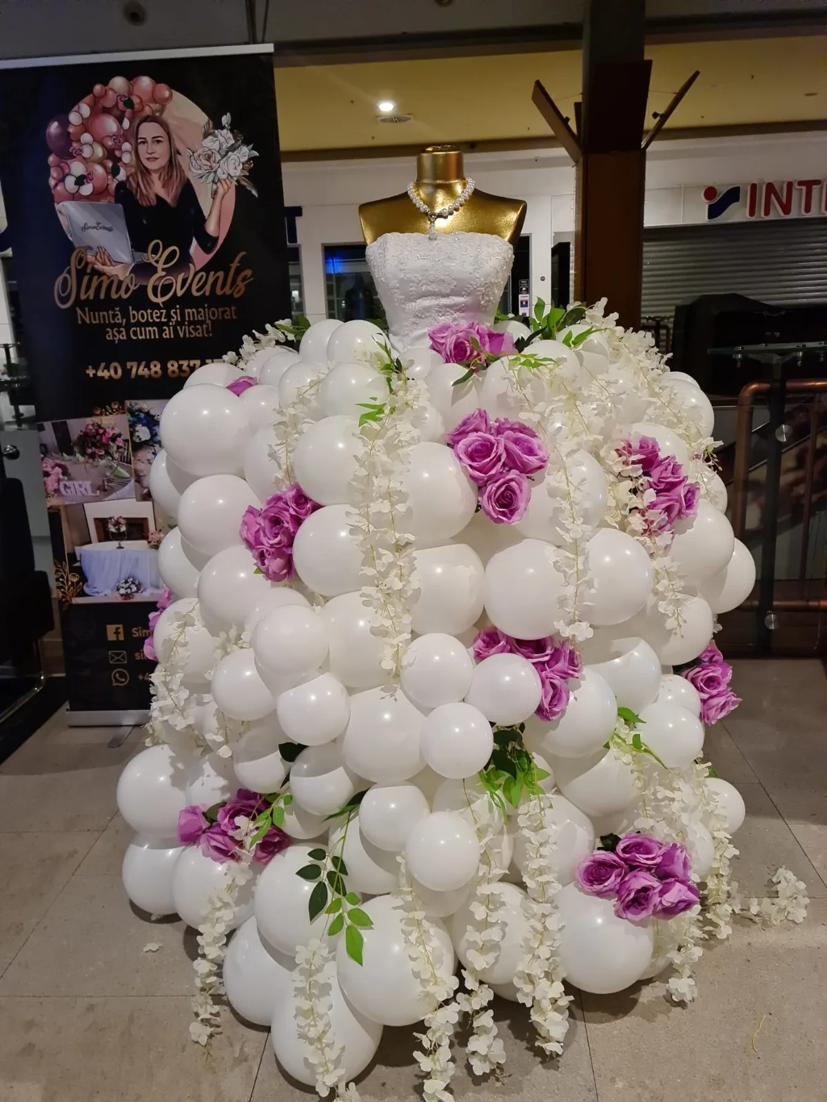 Rochie din baloane albe cu trandafiri mov și glicină, pe manechin cu rochie tip mireasă