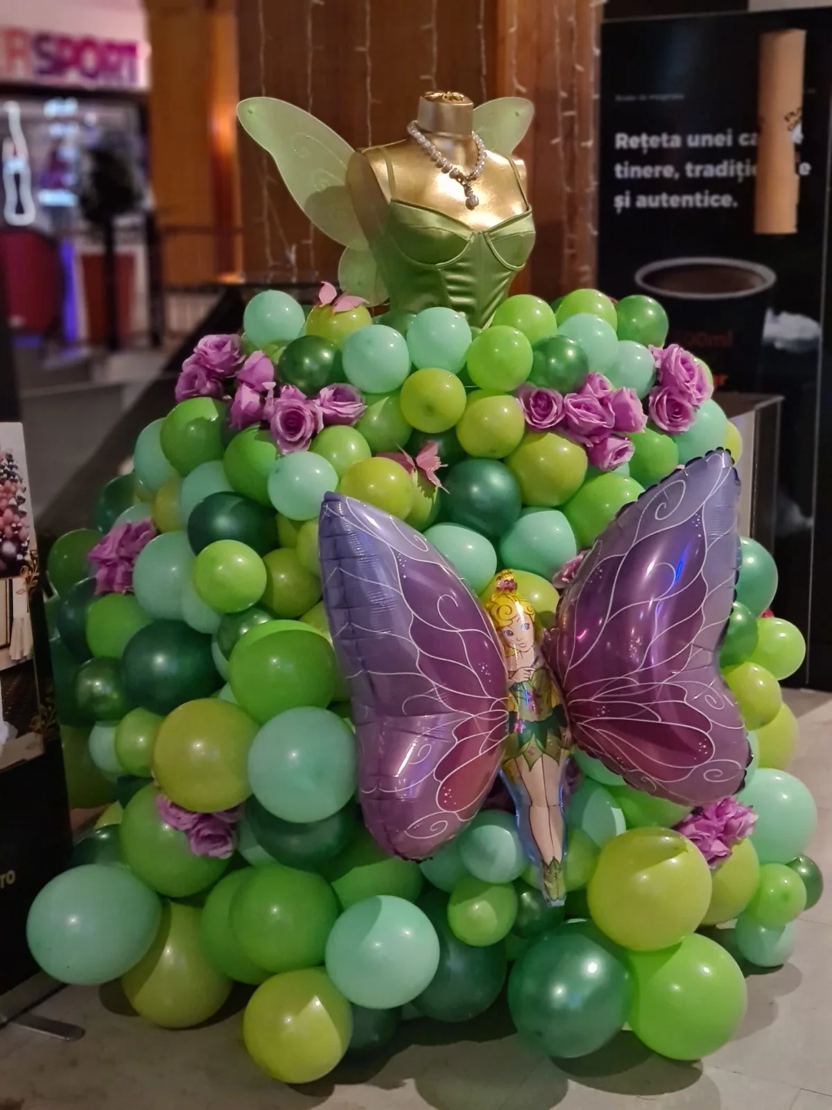 Rochie din baloane verzi cu trandafiri mov și balon fluture mov uriaș, pe manechin cu corset verde și aripi