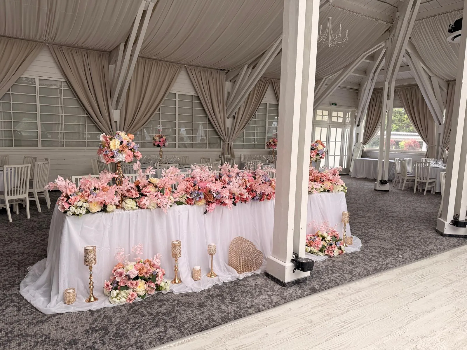 Masa prezidiului cu flori roz-pastel, draperii bej și stâlpi albi, Sala Aldi Gura Humorului