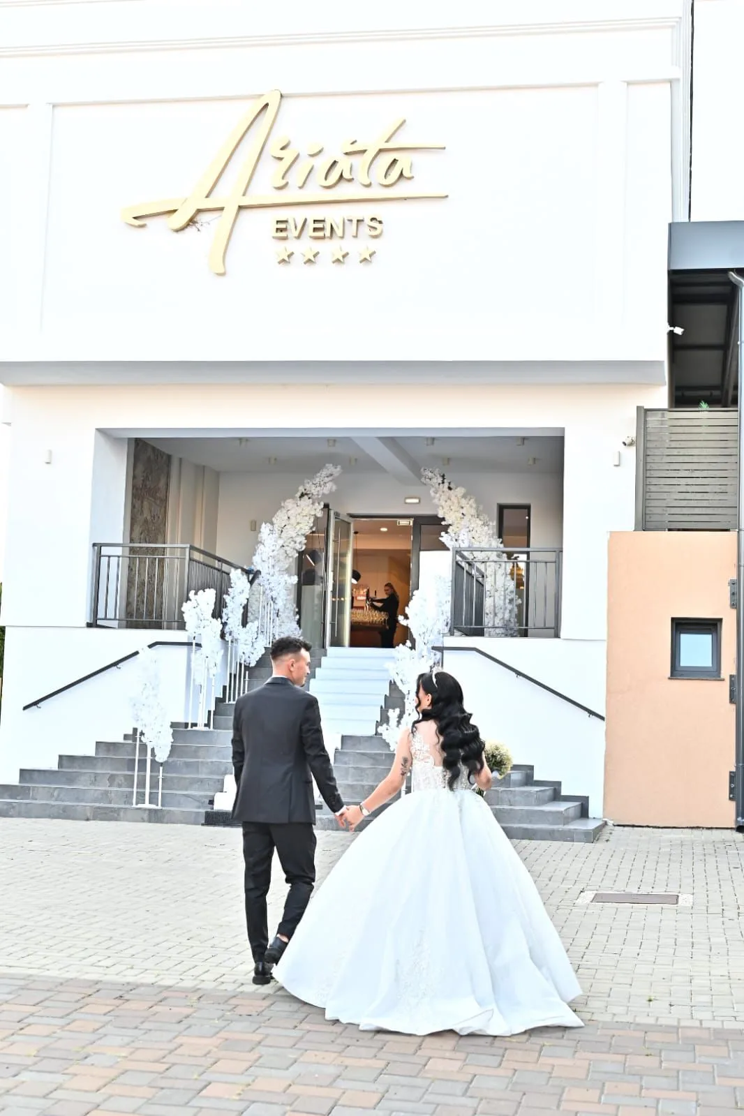 Intrarea salii Ariata Events, cu scari decorate cu arcade florale albe, mire si mireasa urcand spre intrare