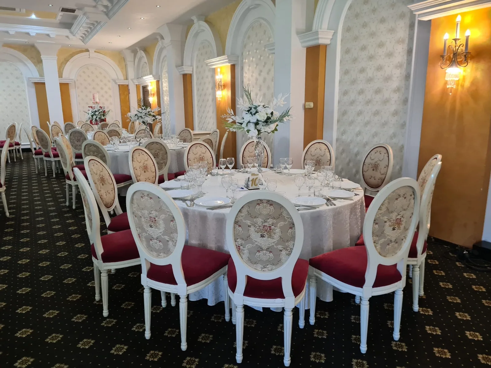Sala Zamca amenajata pentru nunta, mese rotunde cu fete de masa albe si aranjamente florale albe