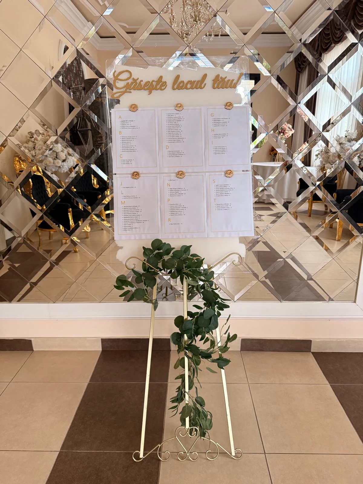 Șevalet auriu cu plan de așezare a invitaților la mese, decorat cu verdeață de eucalipt