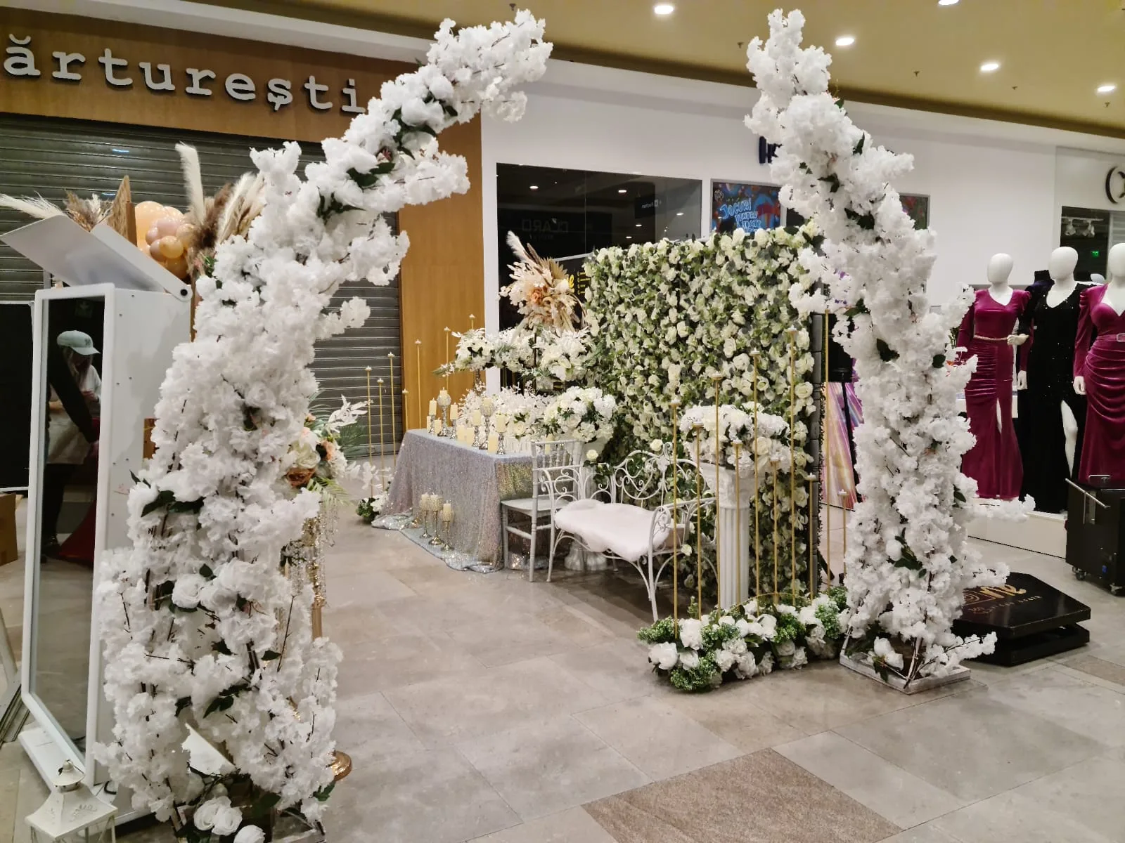 Arcada florala alba dubla langa perete verde floral si banca alba la targul de nunti