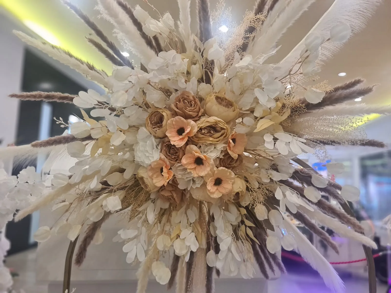 Detaliu aranjament floral cu pene, flori piersica si frunze uscate la targul de nunti