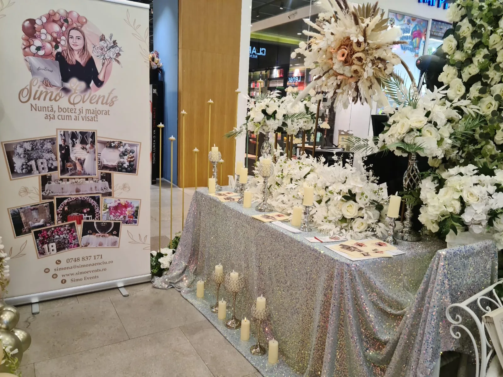 Masa cu fata argintie, roll-up SimoEvents si lumanari albe la targul de nunti