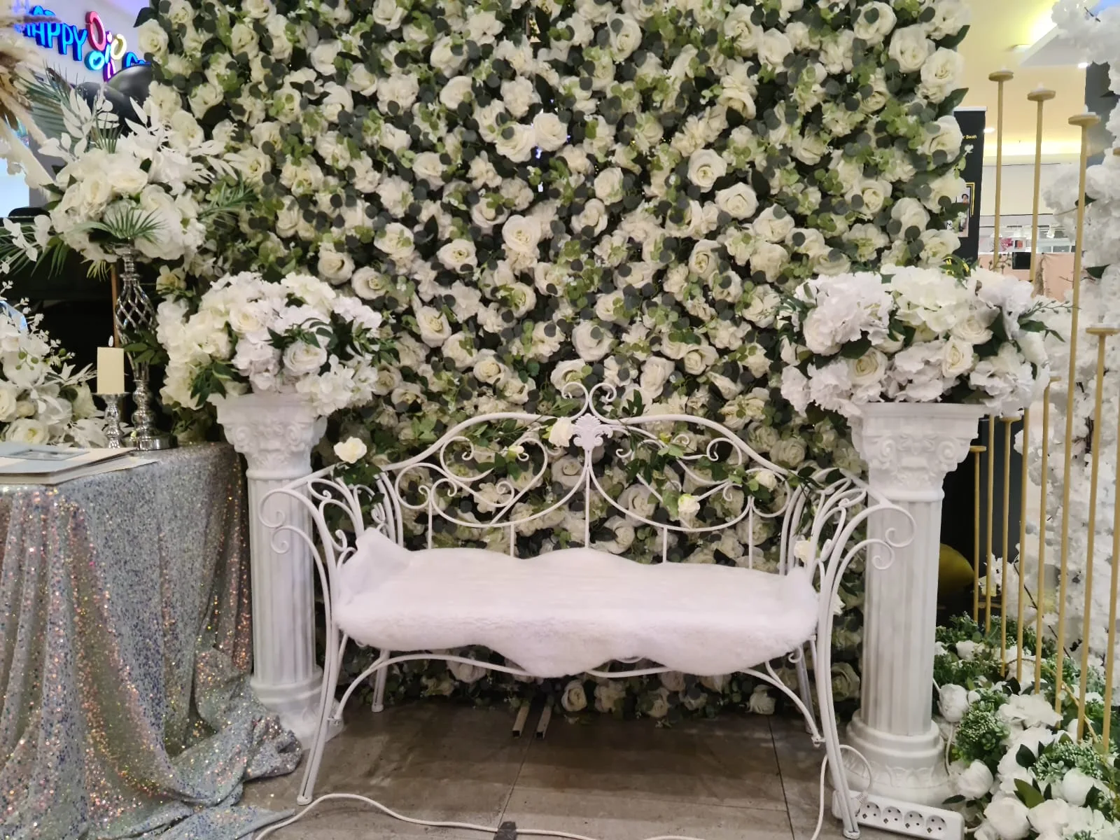 Perete floral alb-verde cu banca alba metalica si coloane albe la targul de nunti
