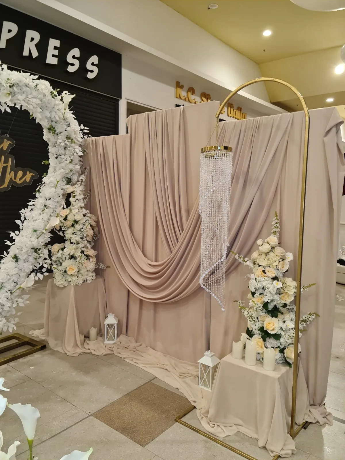Arcadă aurie cu cerc floral alb, draperie bej cu paiete și felinare albe la bază