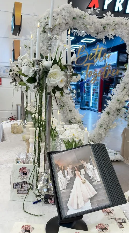 Candelabru auriu cu lumânări și flori albe, lângă inimă florală și ramă foto cu mireasa