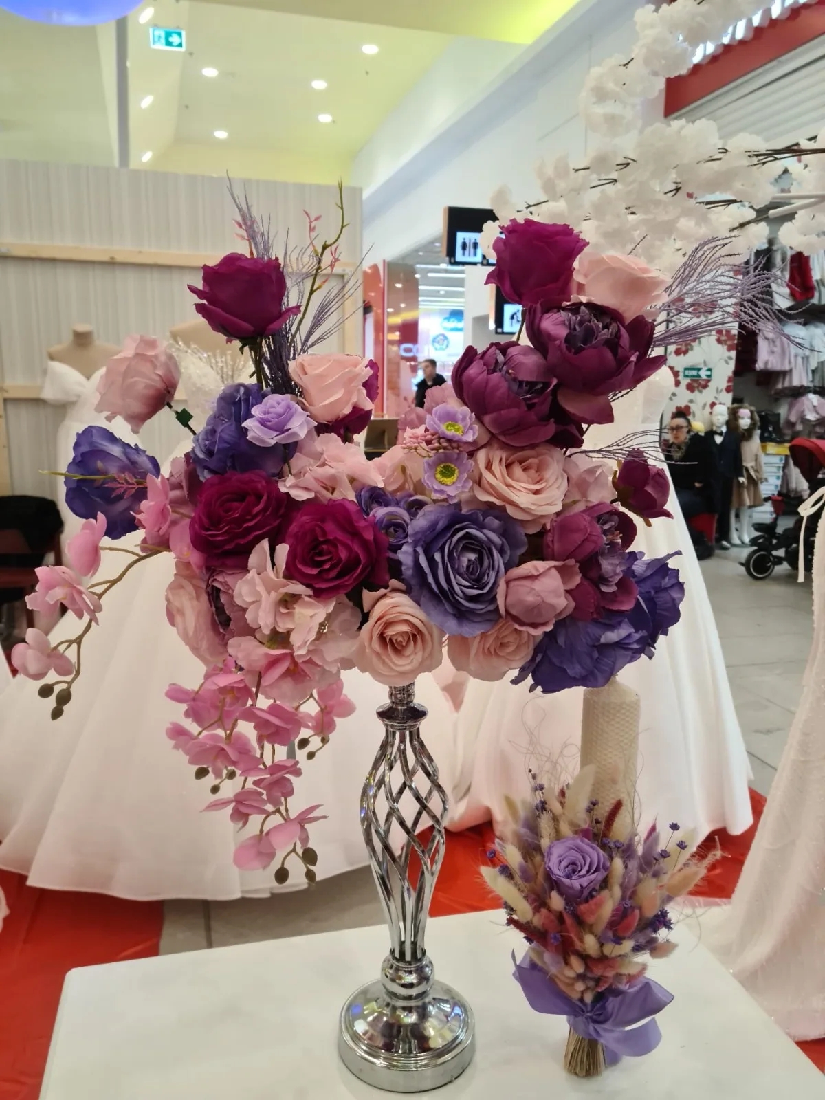 Aranjament floral mov si roz intr-o vaza argintie, pe masa cu fata alba