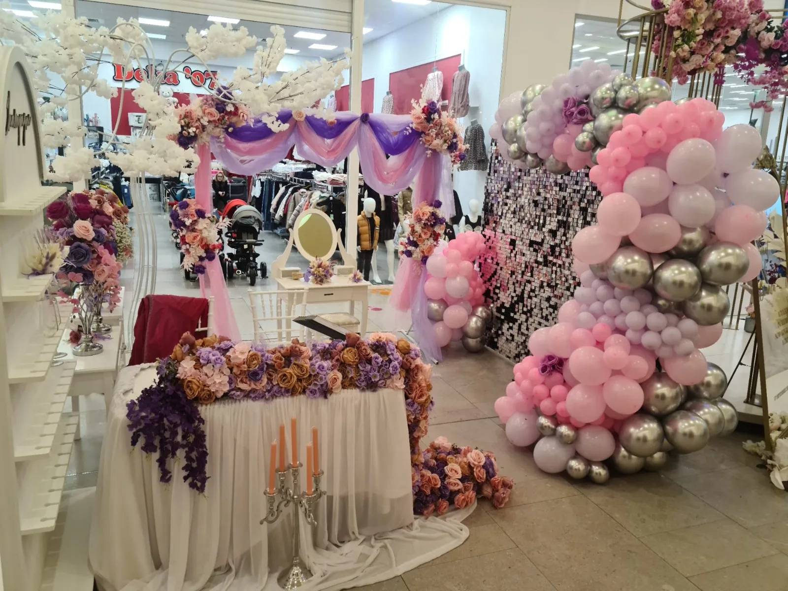 Culoar cu decor floral, draperii mov si ciucure de baloane roz-argintii la targul de nunti