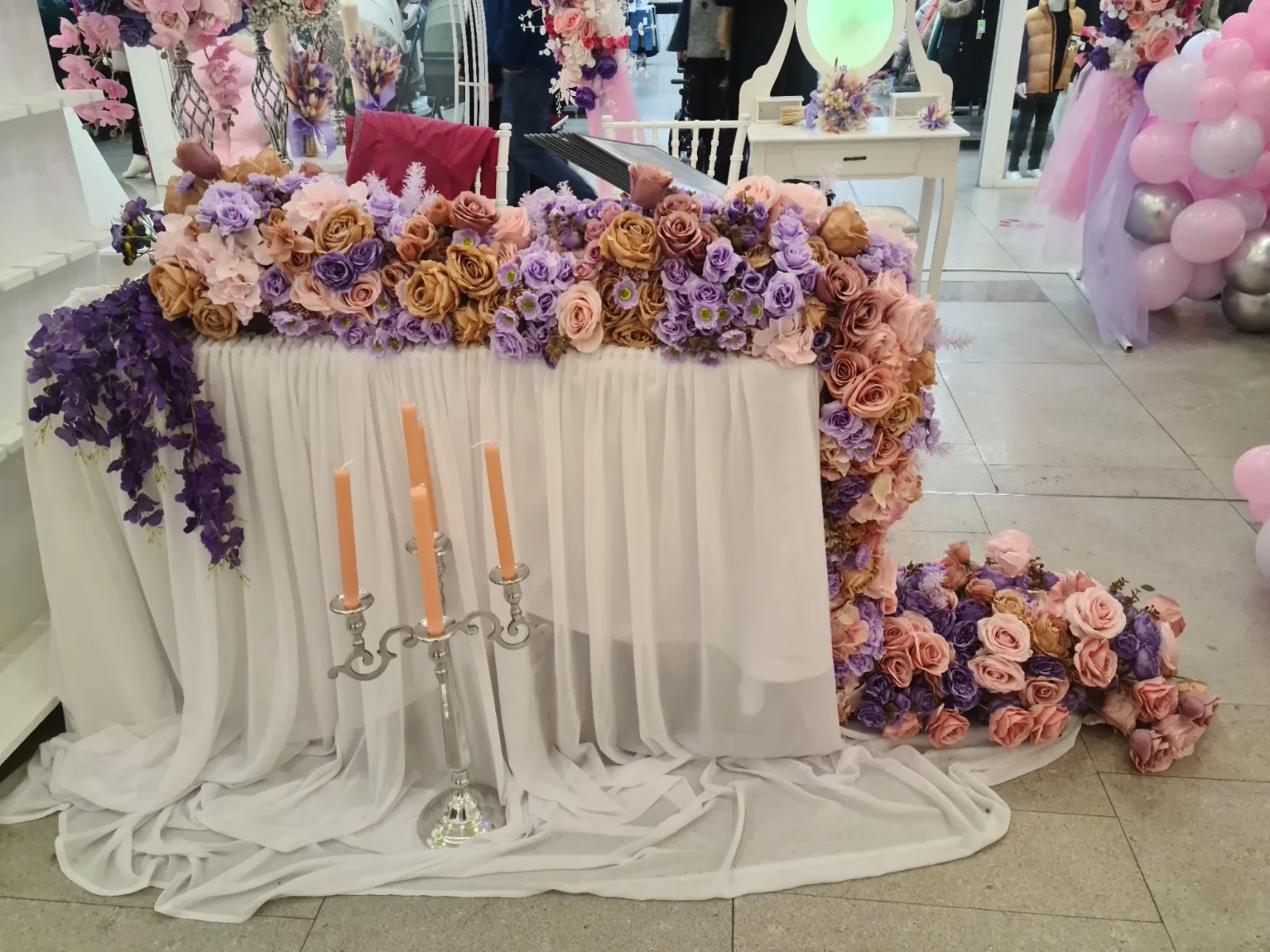 Masa decorata cu flori mov, roz si aurii, draperie alba si candelabru cu lumanari